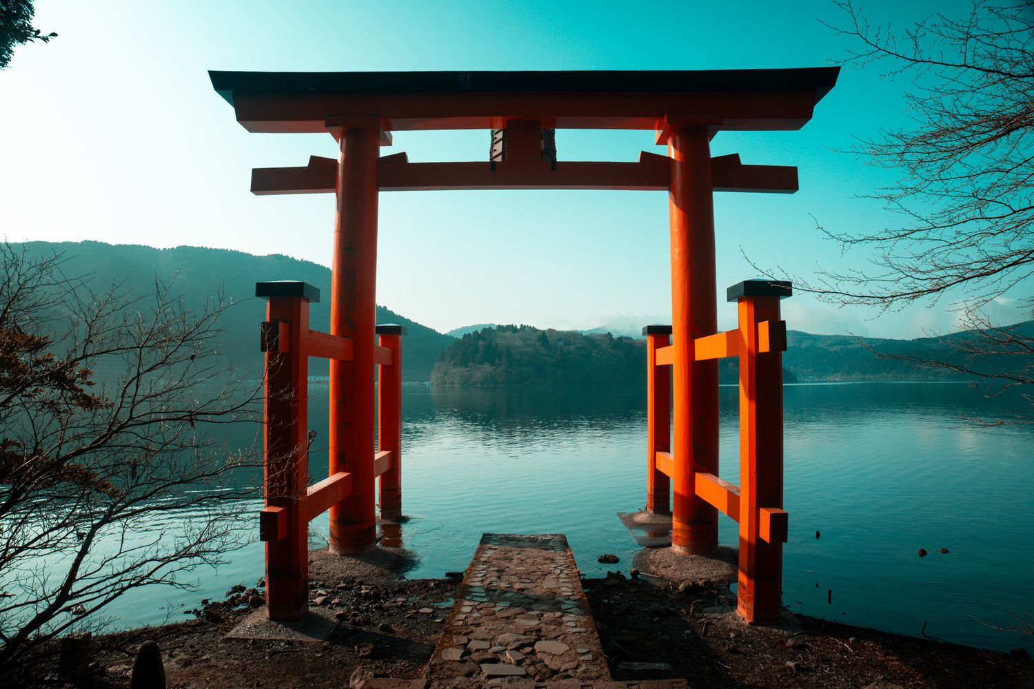 Red torii gate stands over serene lake with misty mountains in background at Japanese Shinto shrine.