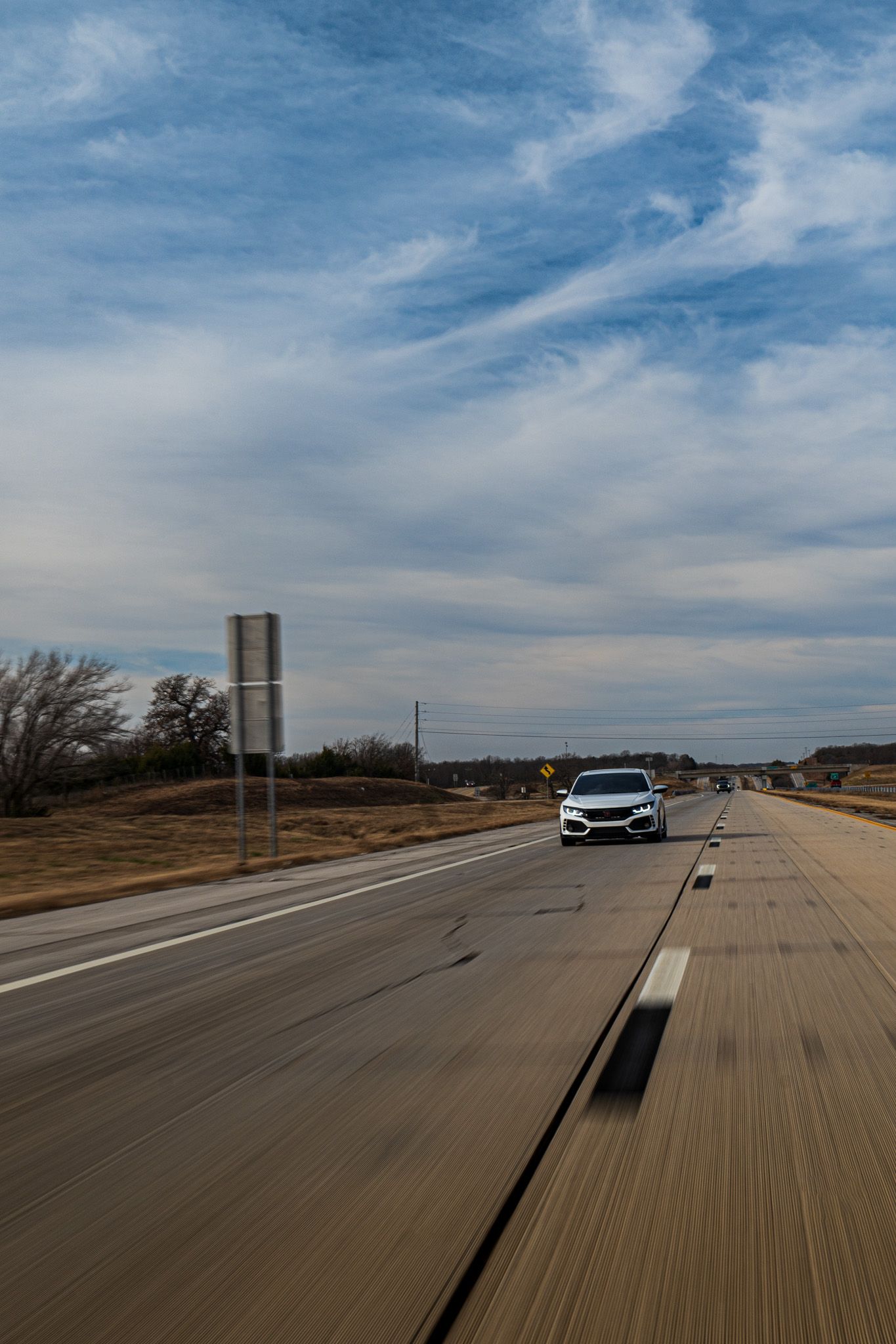 A series of five sequential photos showing a car driving along a rural highway under blue skies with wispy clouds.