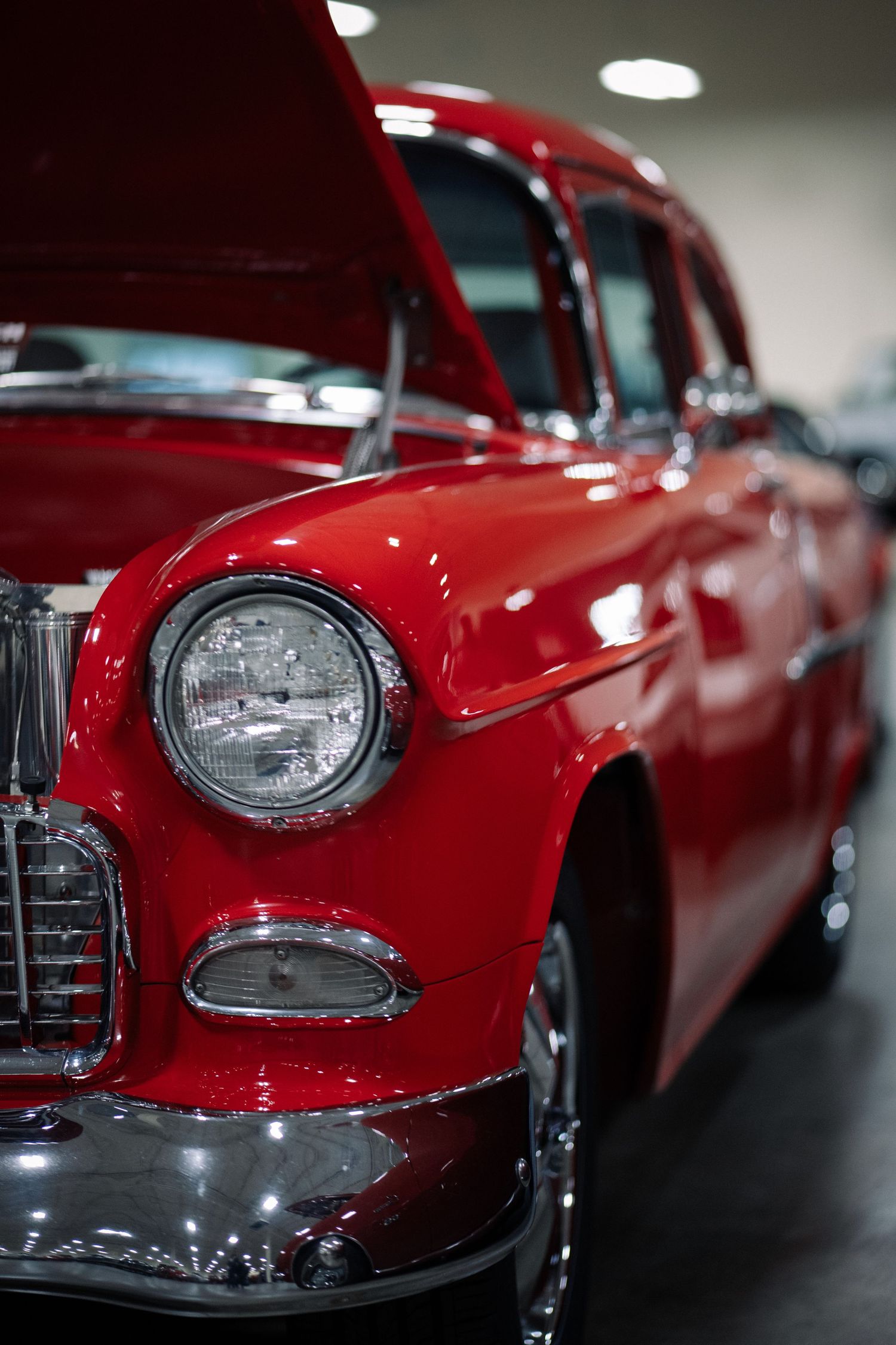 Classic red car front end showing chrome headlights and grille details in showroom lighting.