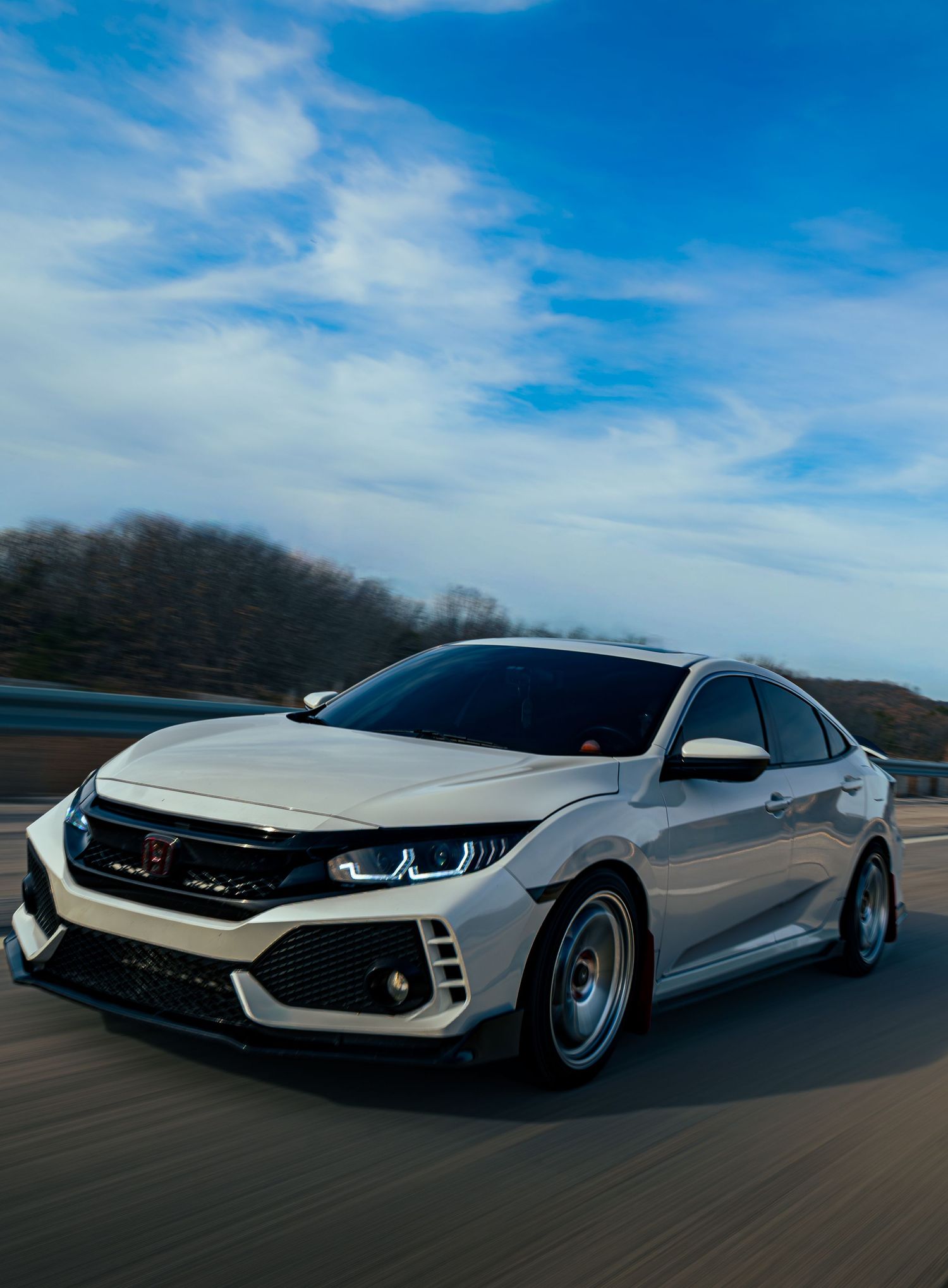 Silver sports car with aggressive wide body styling and sleek aerodynamic design shown in motion against blue sky.