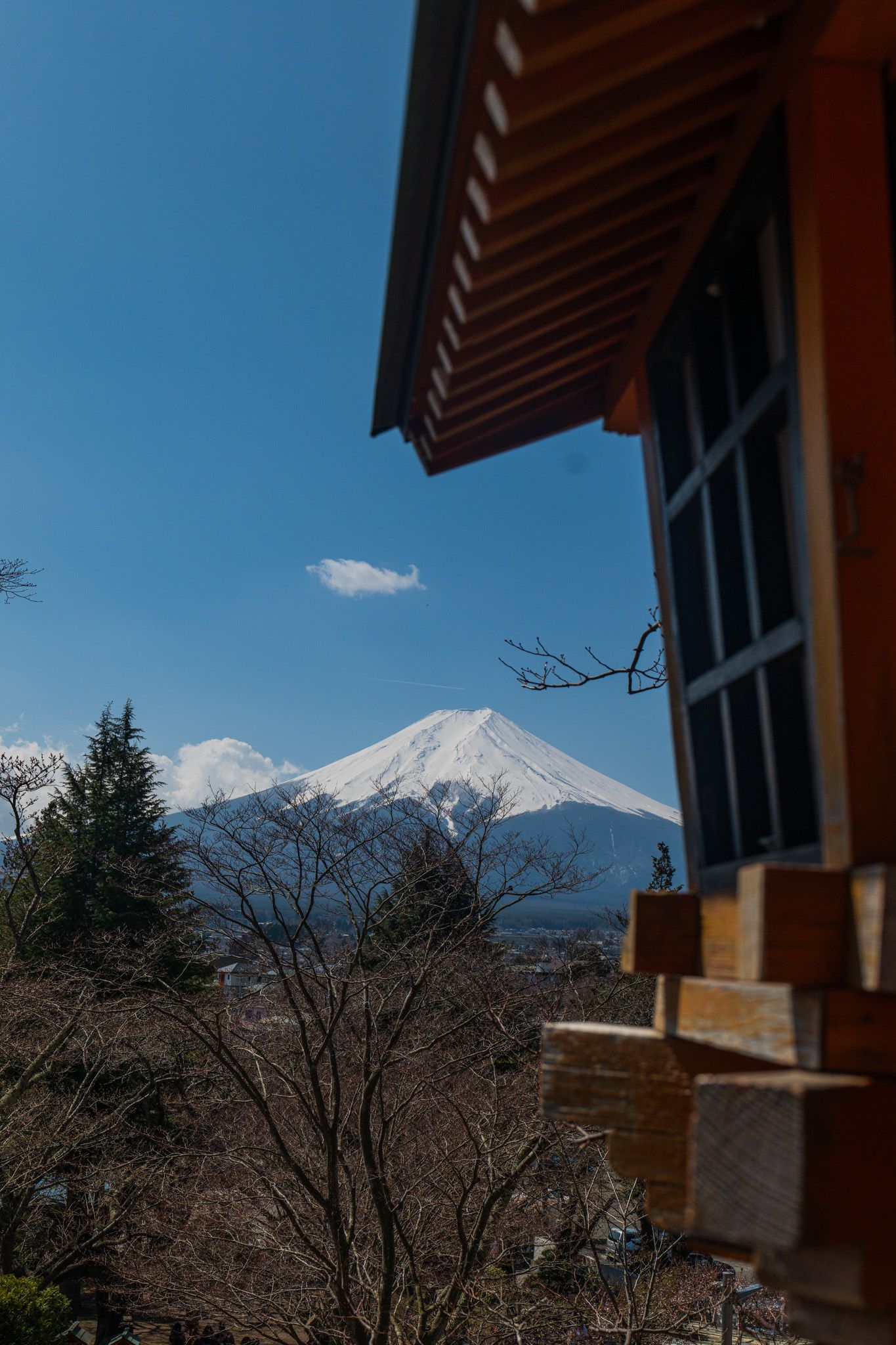 Snow-capped Mount Fuji viewed from a traditional Japanese wooden building on a clear blue day.