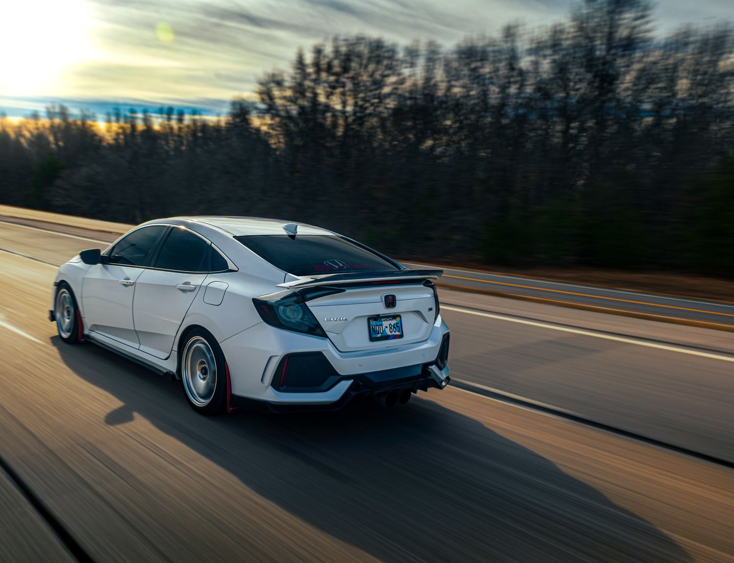 White Honda Civic Type R driving on a highway during sunset with trees in the background.