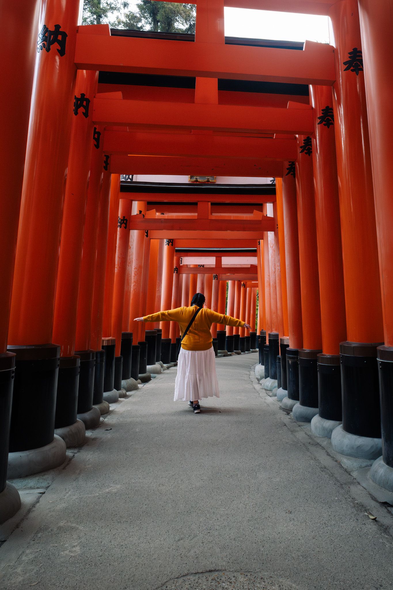 Woman with arms outstretched walking through iconic red torii gates at Fushimi Inari Shrine in Kyoto, Japan.