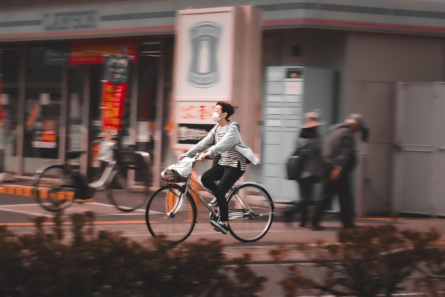 A woman rides an orange bicycle through a busy urban street, wearing a light jacket and black pants.