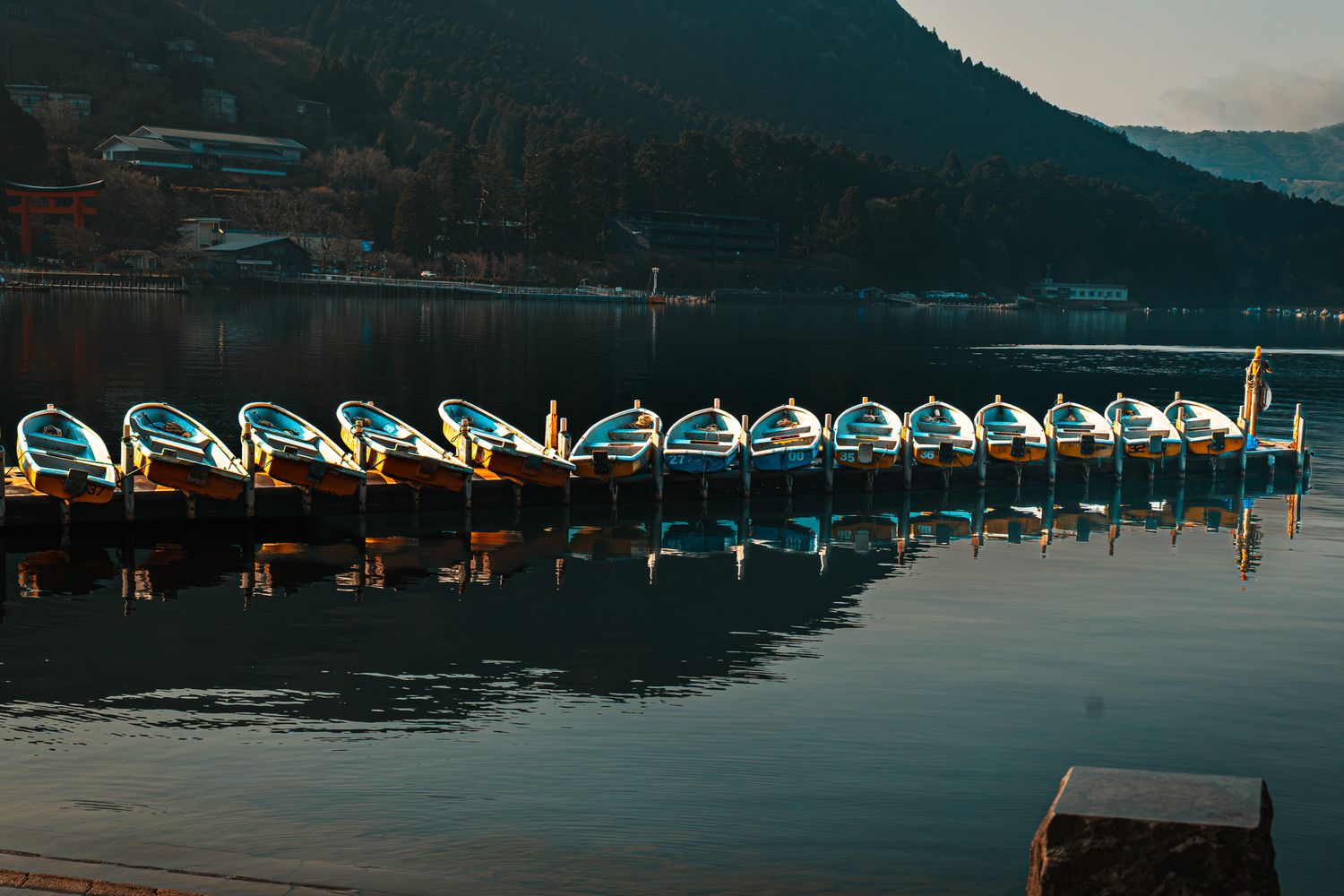 Colorful pedal boats moored in a row on a calm mountain lake at dusk.