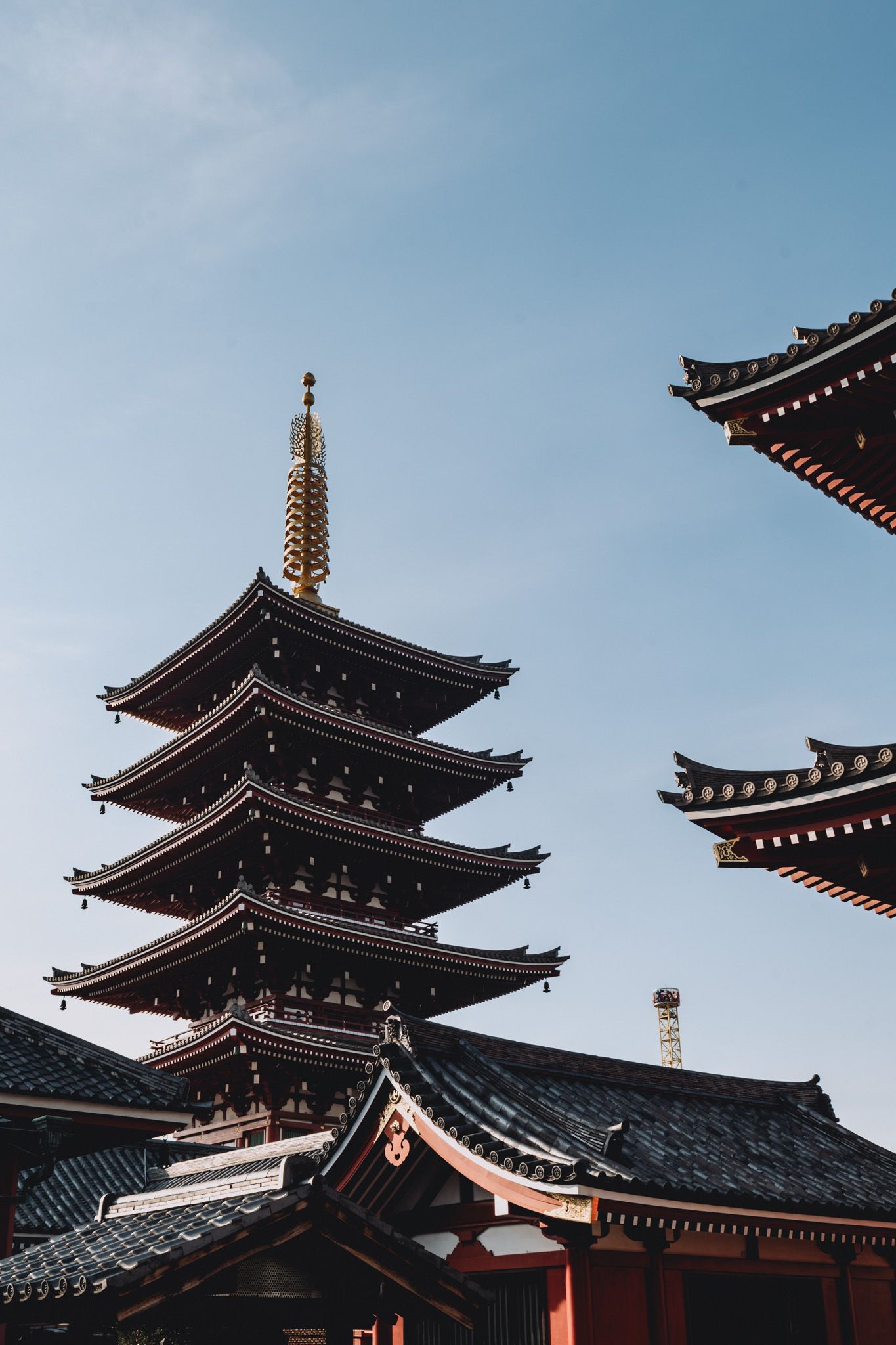 Traditional Japanese five-story pagoda with golden spire against a clear blue sky in Tokyo.