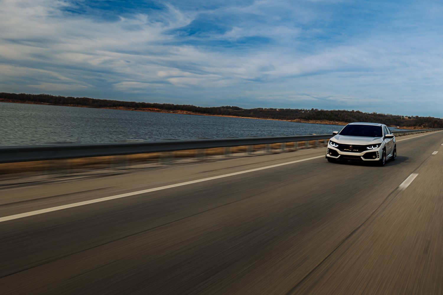 A white Mercedes-Benz SUV drives along a coastal highway with blue skies and ocean views stretching to the horizon.