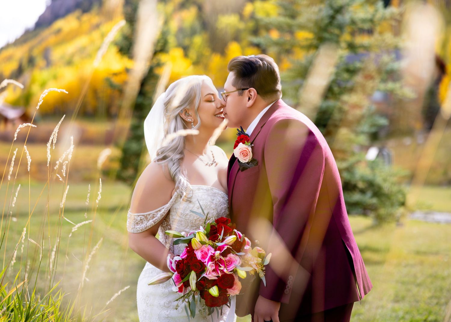 Bride and groom sharing a kiss surrounded by golden autumn trees at outdoor mountain wedding.