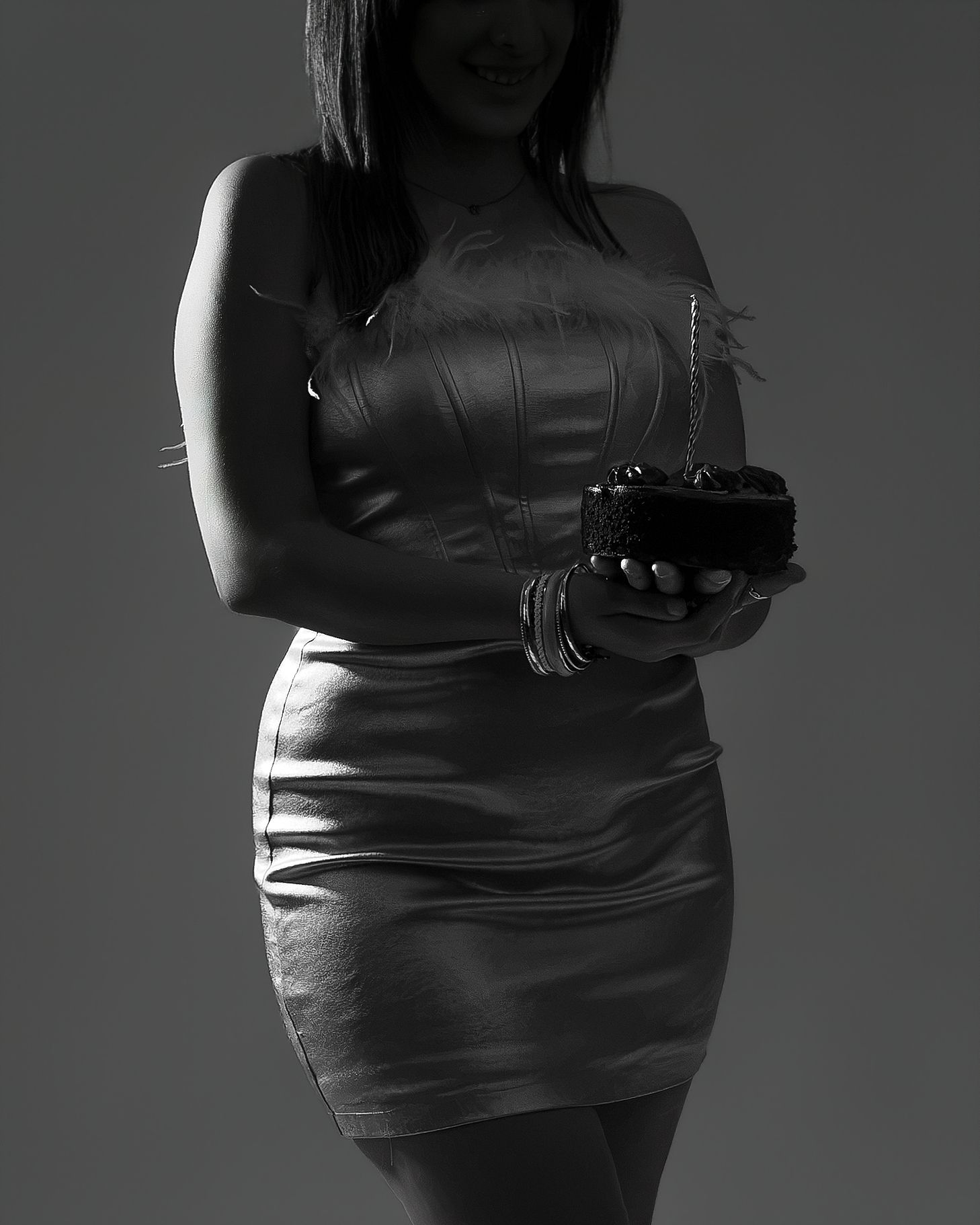 Black and white photo of a woman in a strapless leather mini dress holding a small clutch purse.