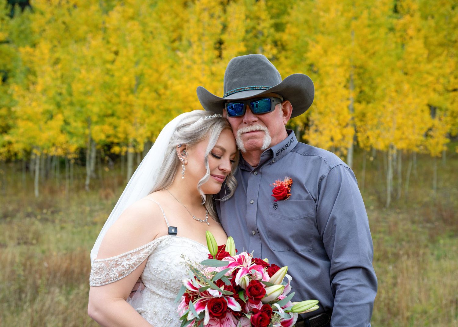 Bride leaning on father figure in cowboy hat among golden aspen trees at autumn wedding.