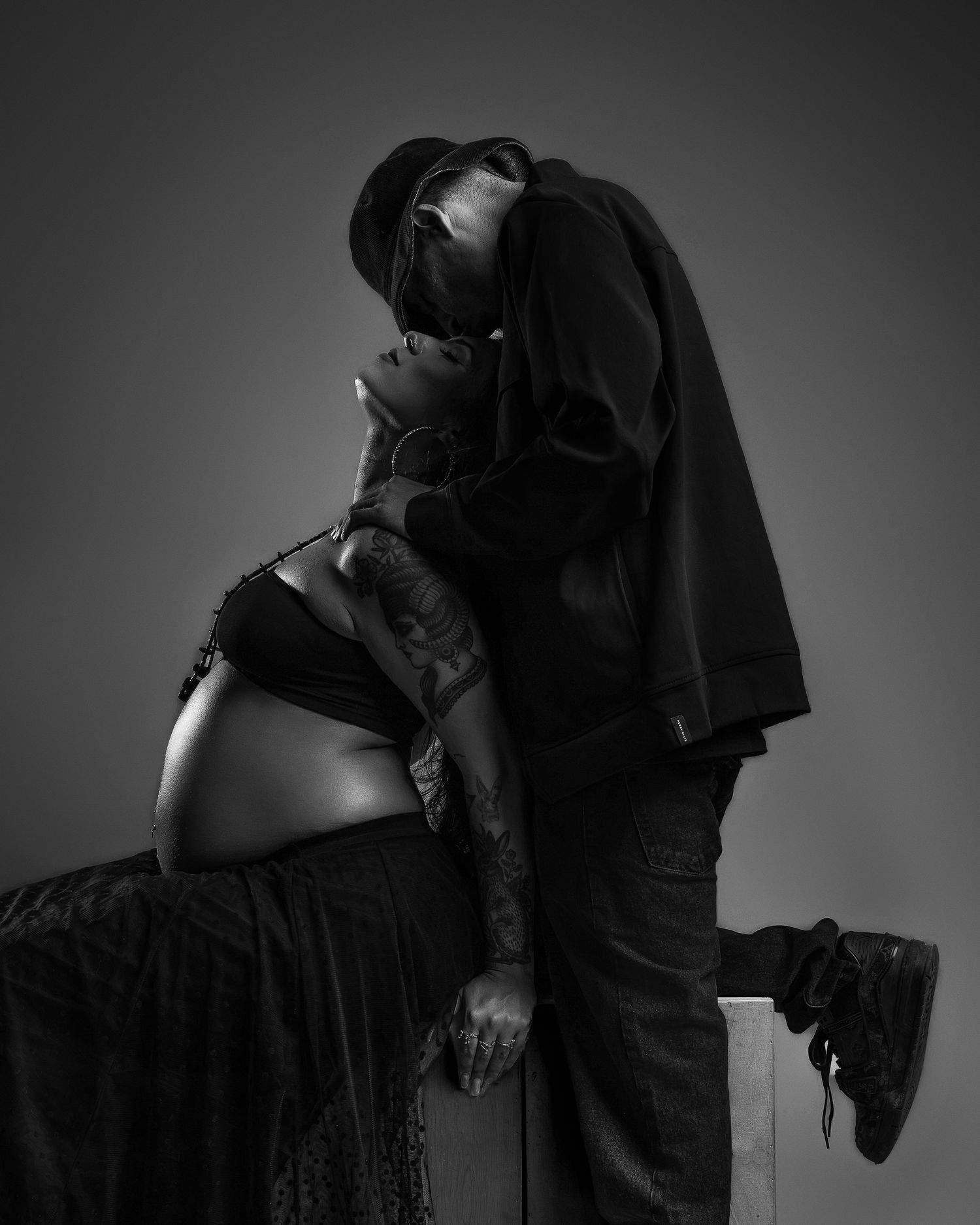 Black and white maternity photo of couple kissing, pregnant woman in black lace skirt.