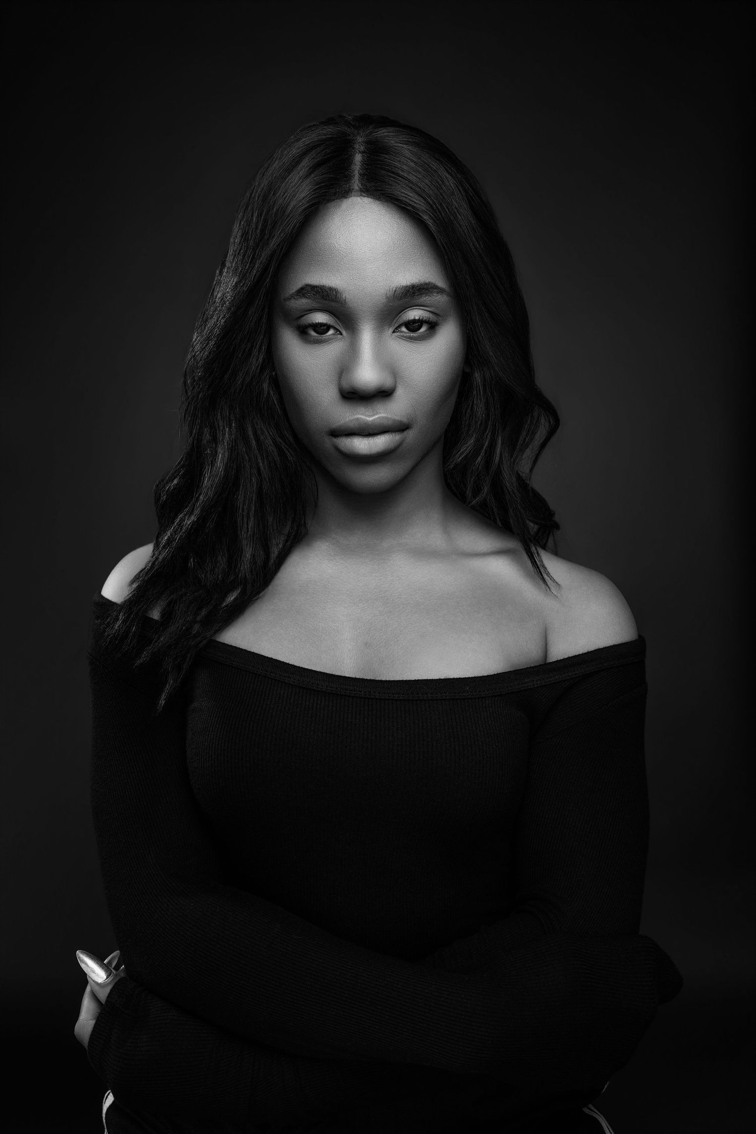 Black and white portrait of a young woman in an off-shoulder top, posing confidently against a dark background.
