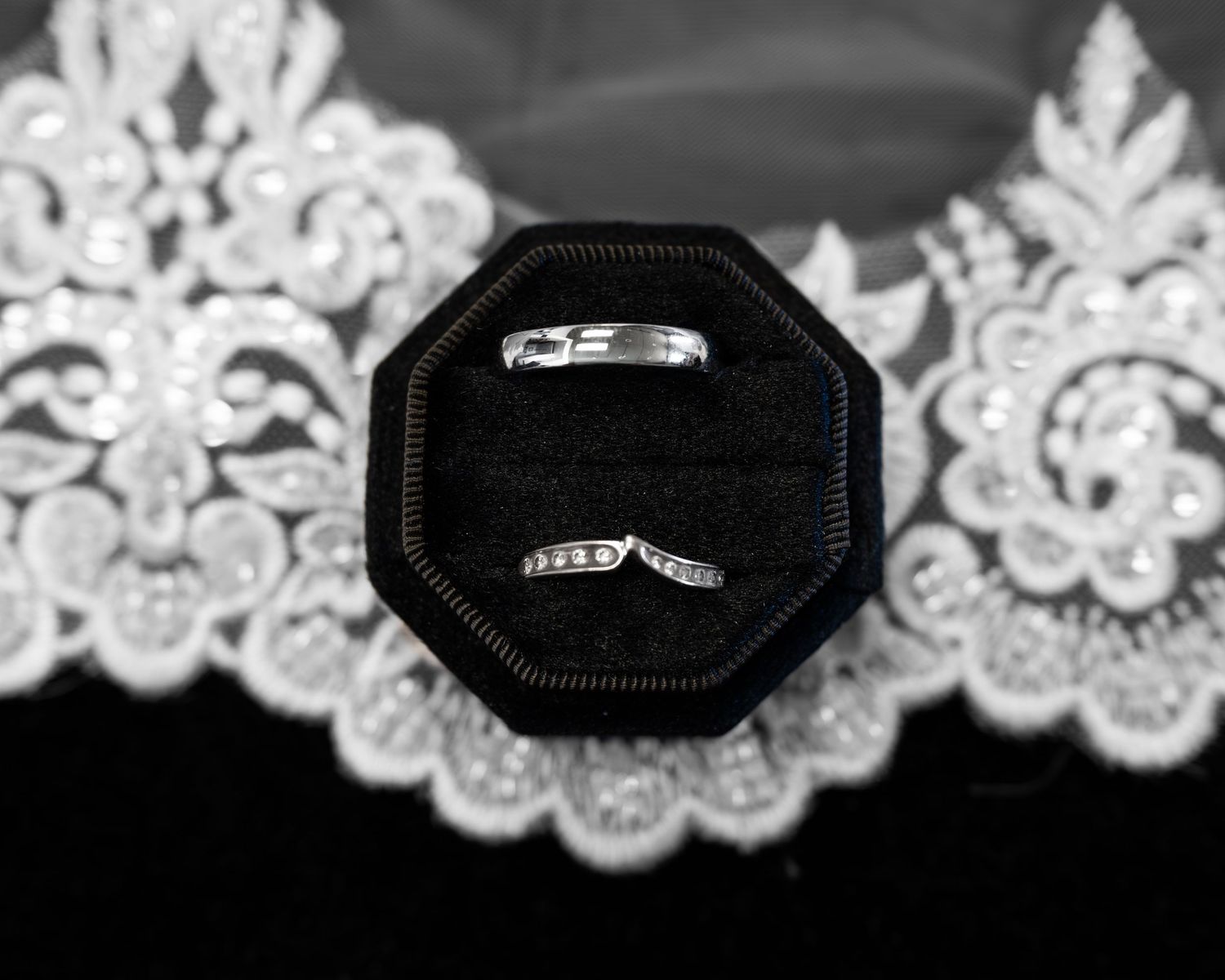 Two silver wedding bands displayed in black velvet ring box on white lace fabric, black and white.