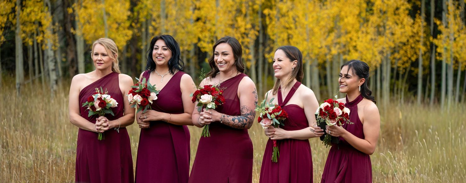 Five bridesmaids in burgundy dresses holding bouquets in front of golden fall aspen trees.