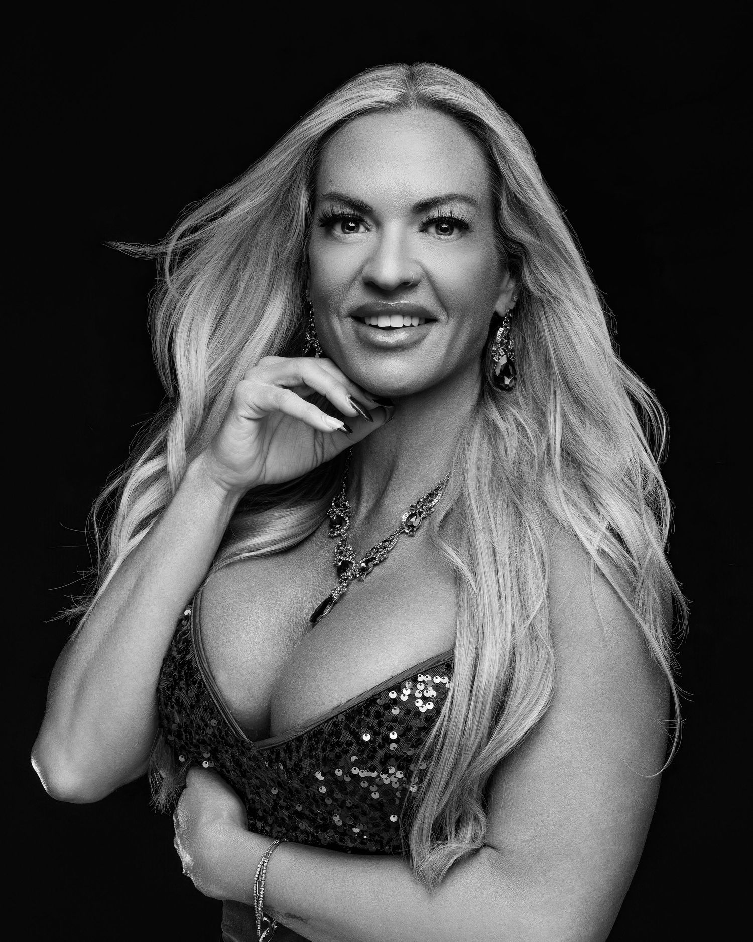Black and white portrait of a blonde woman in a sequined dress with elegant jewelry, posing confidently.