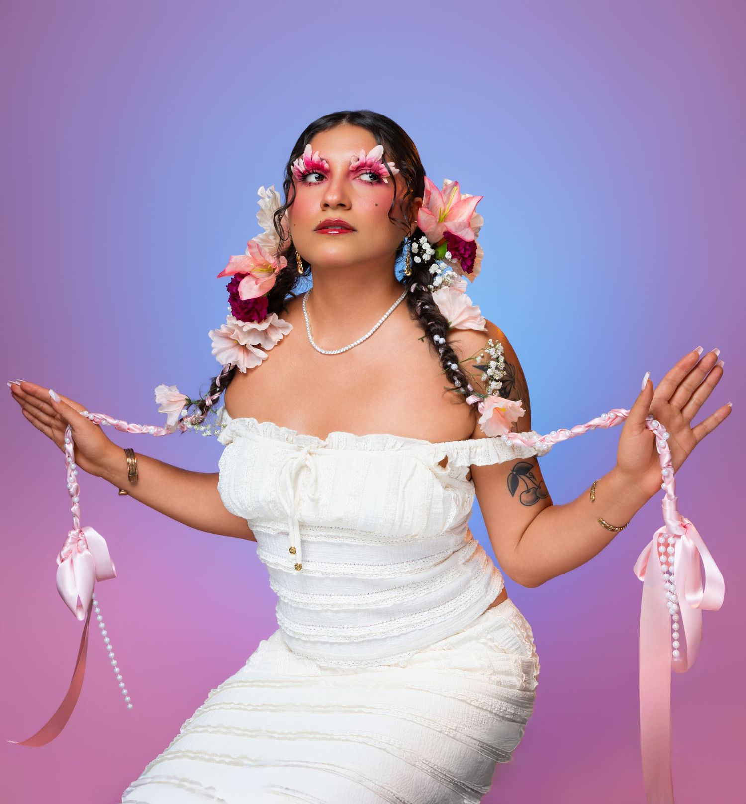 Woman in white strapless dress with floral hair accessories and pink eye makeup holds ribbon against gradient background.