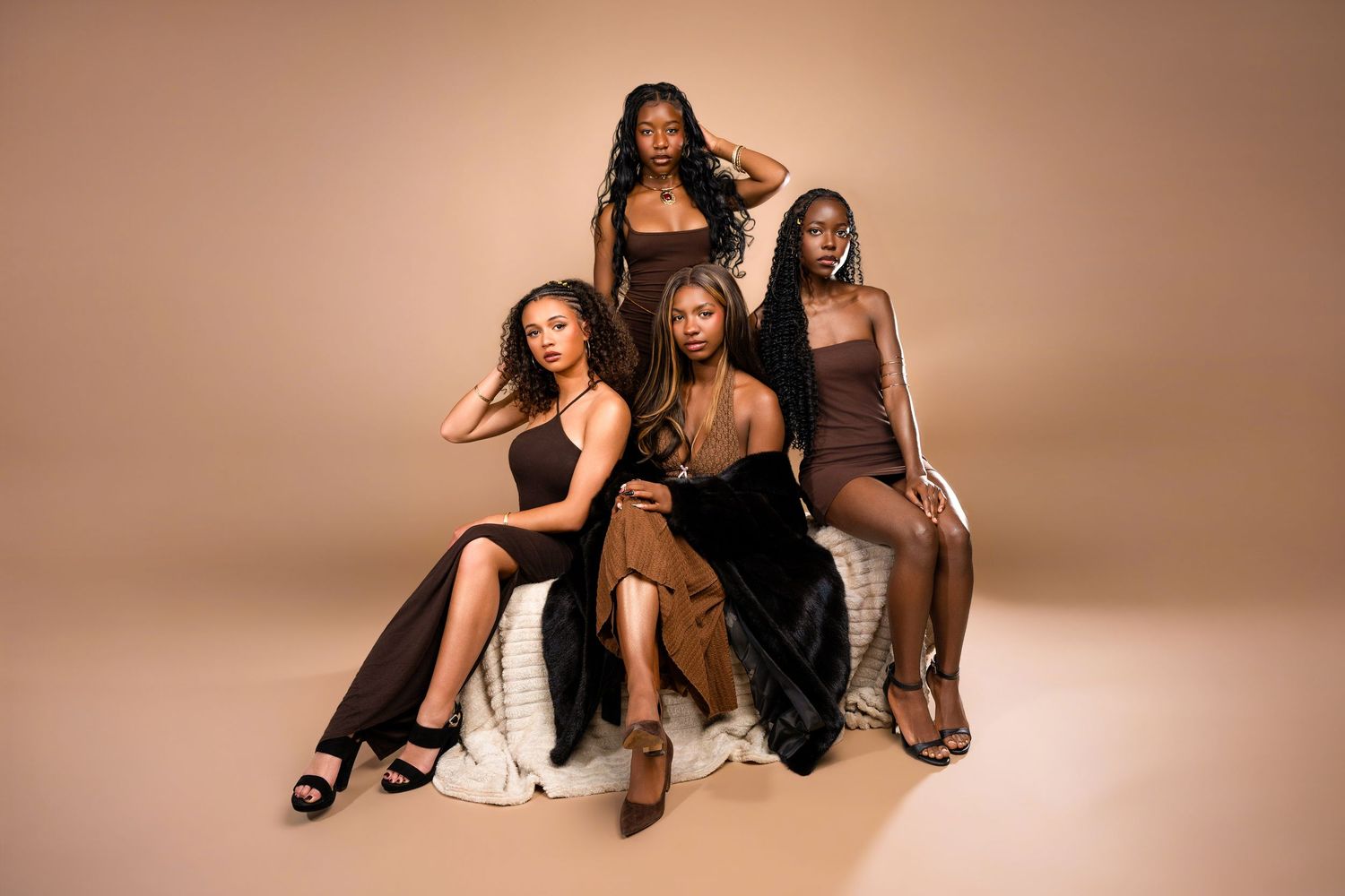 Four women in brown outfits pose together against a beige background in a stylish fashion photoshoot.