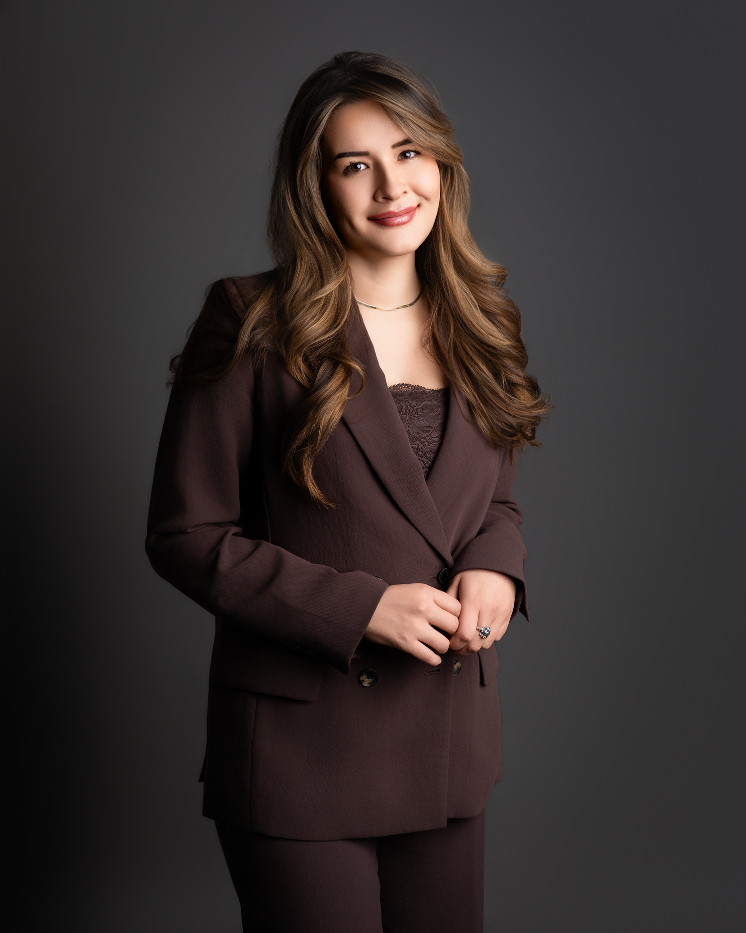 Young professional woman smiling in a burgundy blazer suit against a dark studio background.