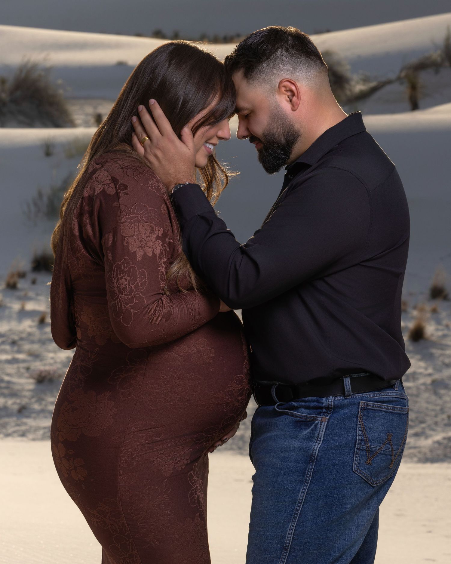 Expecting couple sharing intimate forehead touch during maternity photo session on white sands.