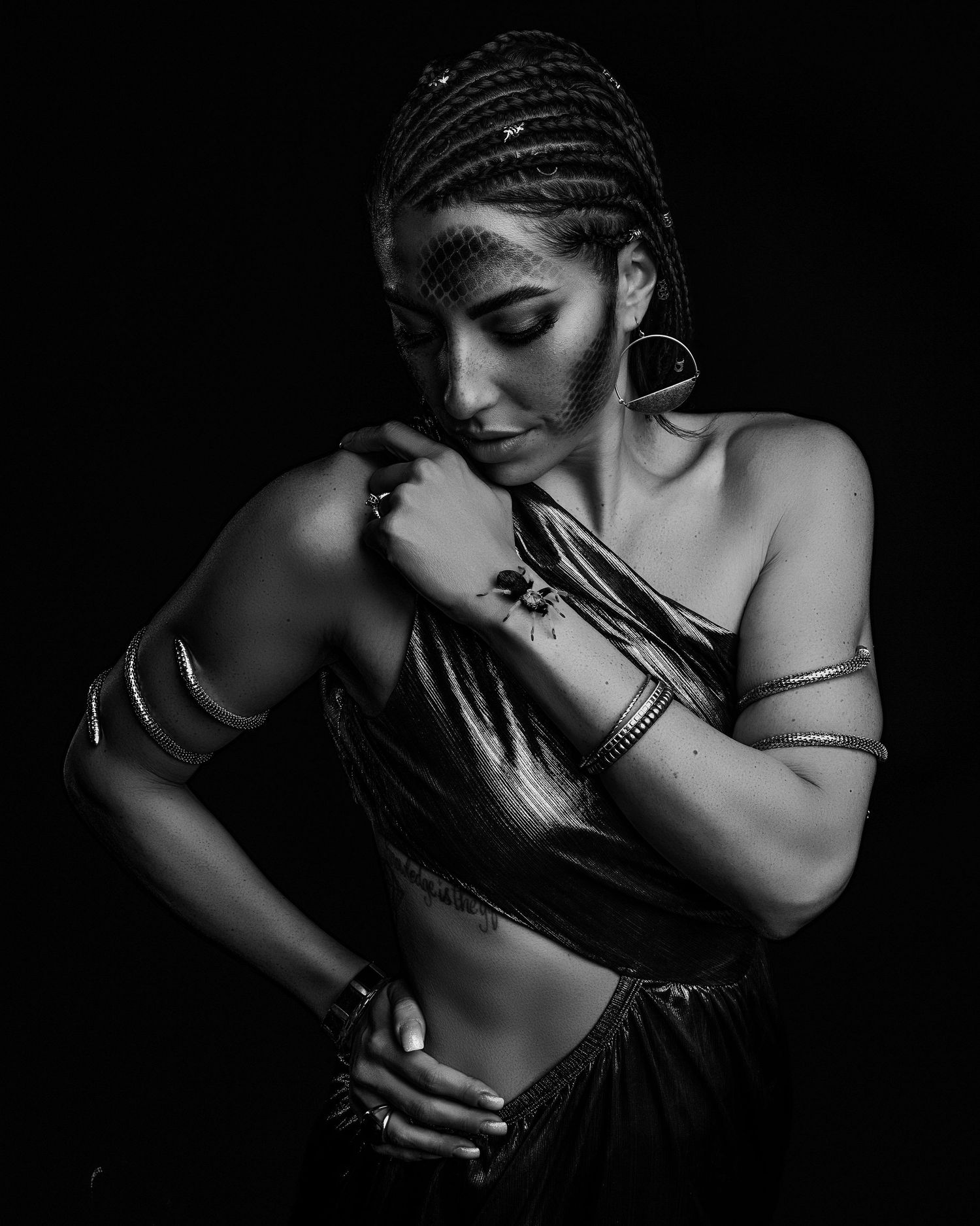 Black and white portrait of a woman with braided hair, jewelry, and a crop top posing dramatically against dark background.