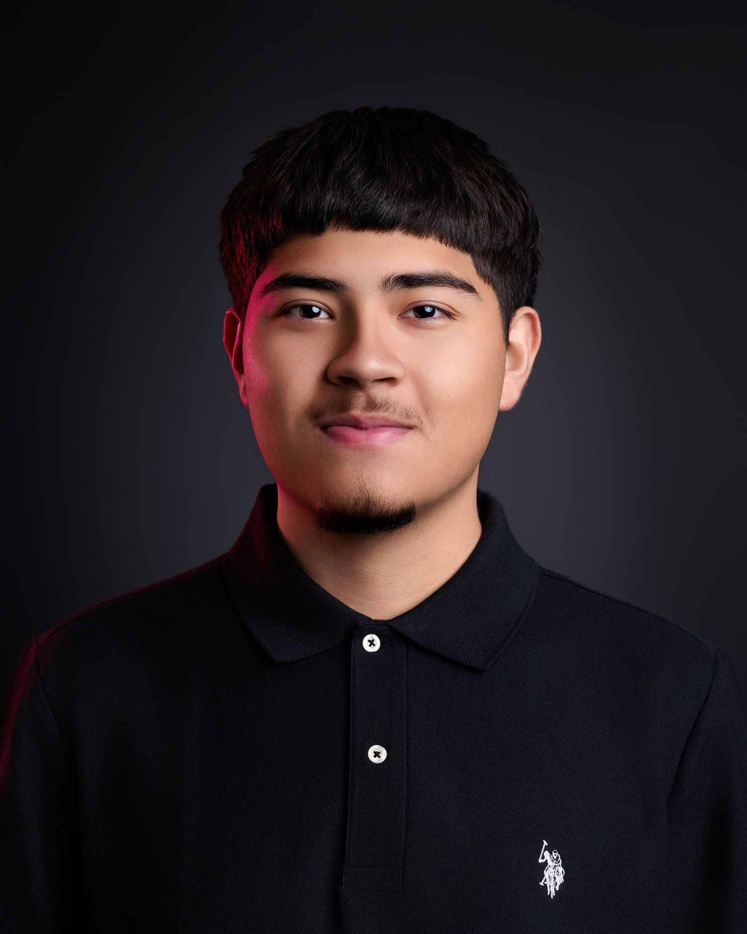 Young man smiling in a black polo shirt against a dark background for a professional portrait photo.