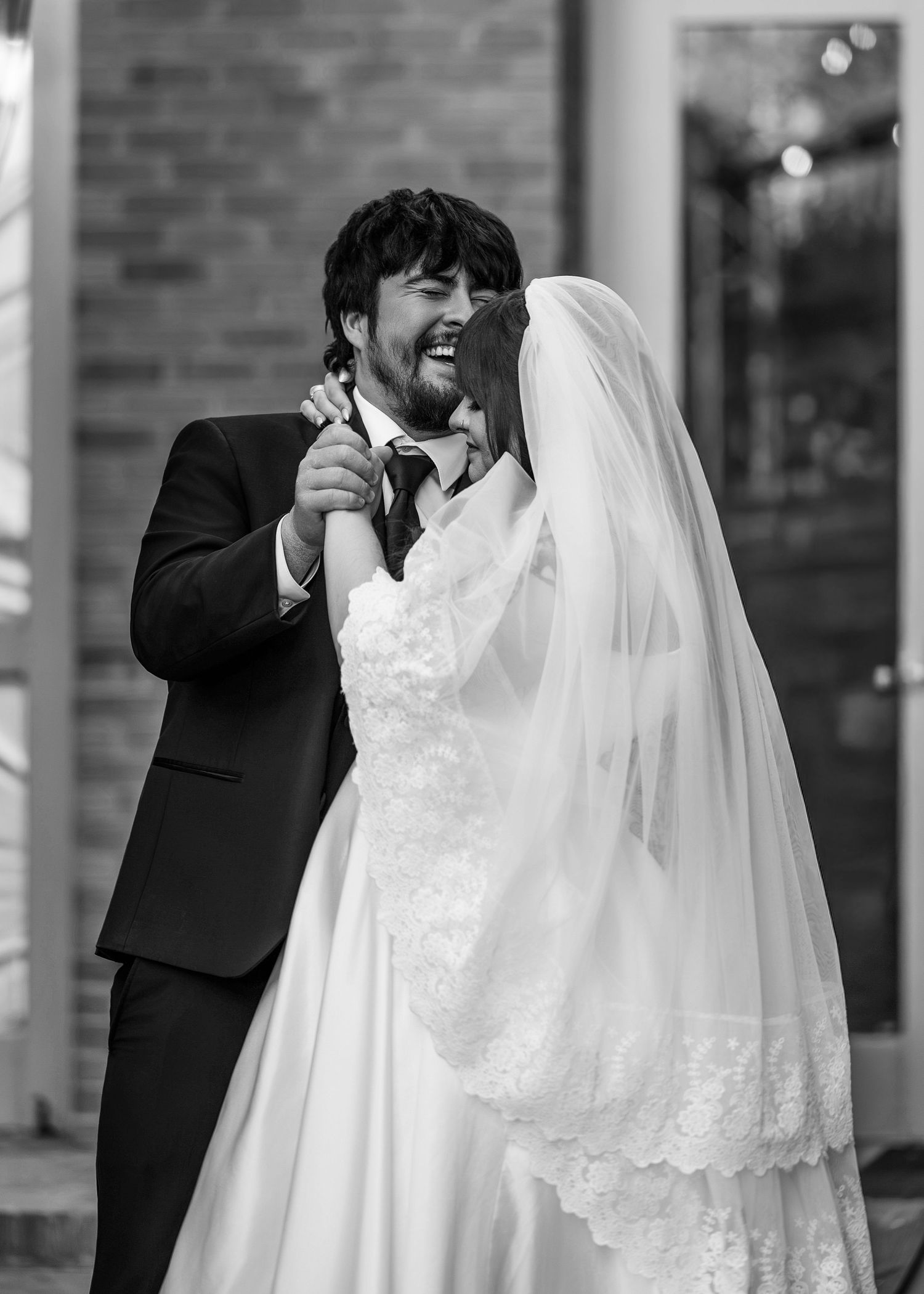 Laughing bride and groom share joyful first dance outdoors in black and white wedding photo.