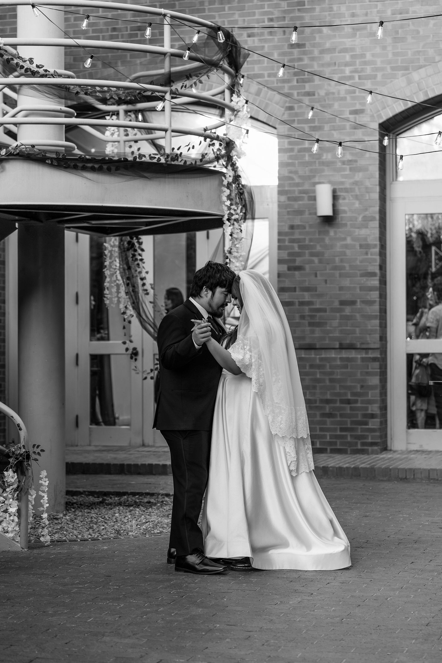Bride and groom share first dance embrace outdoors under string lights at wedding reception venue.