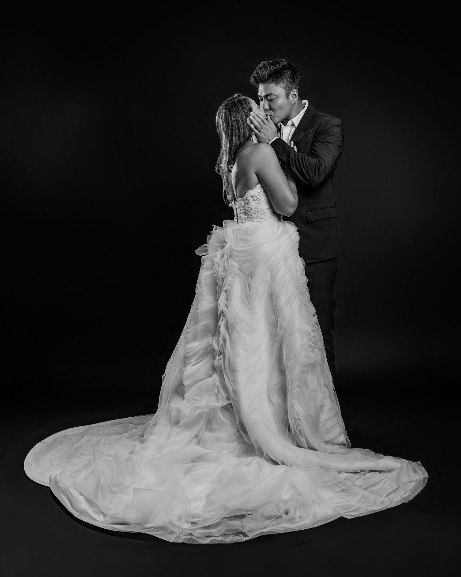 Black and white photo of bride and groom sharing a kiss in elegant wedding attire.