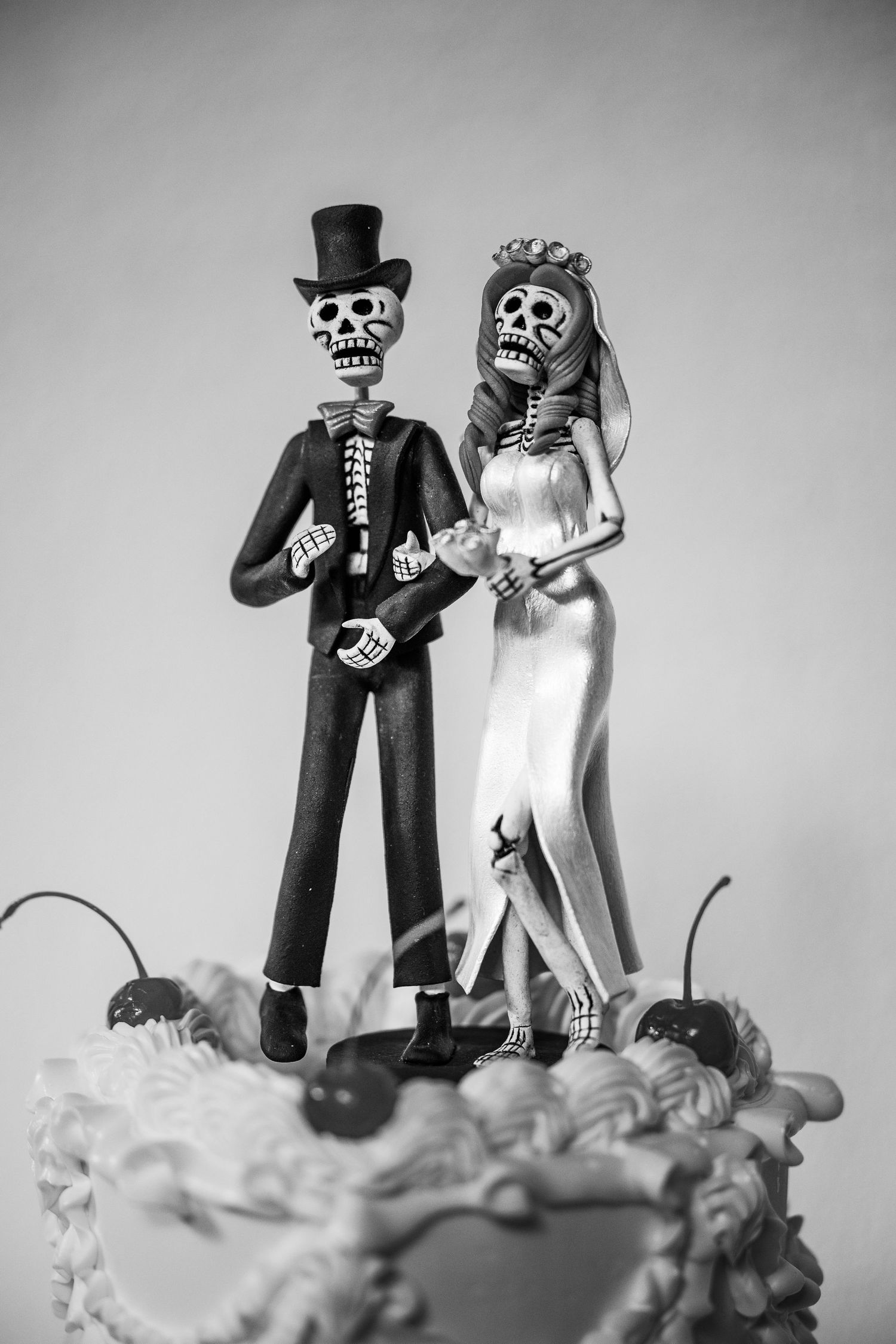 Black and white photo of skeleton bride and groom cake toppers on decorated wedding cake.