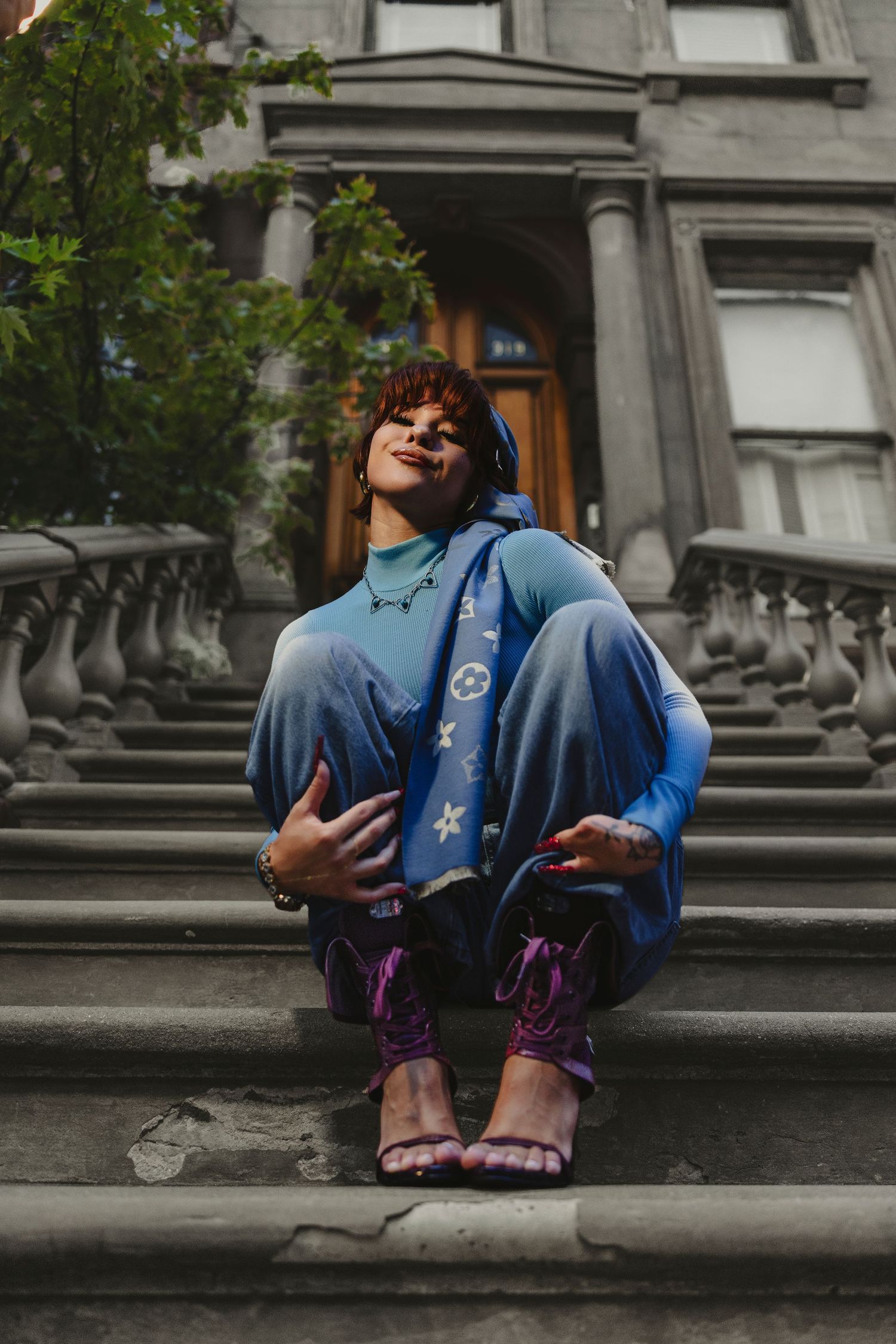 Person in blue outfit and purple heels sitting on stone steps outside a historic building wearing blue headphones.