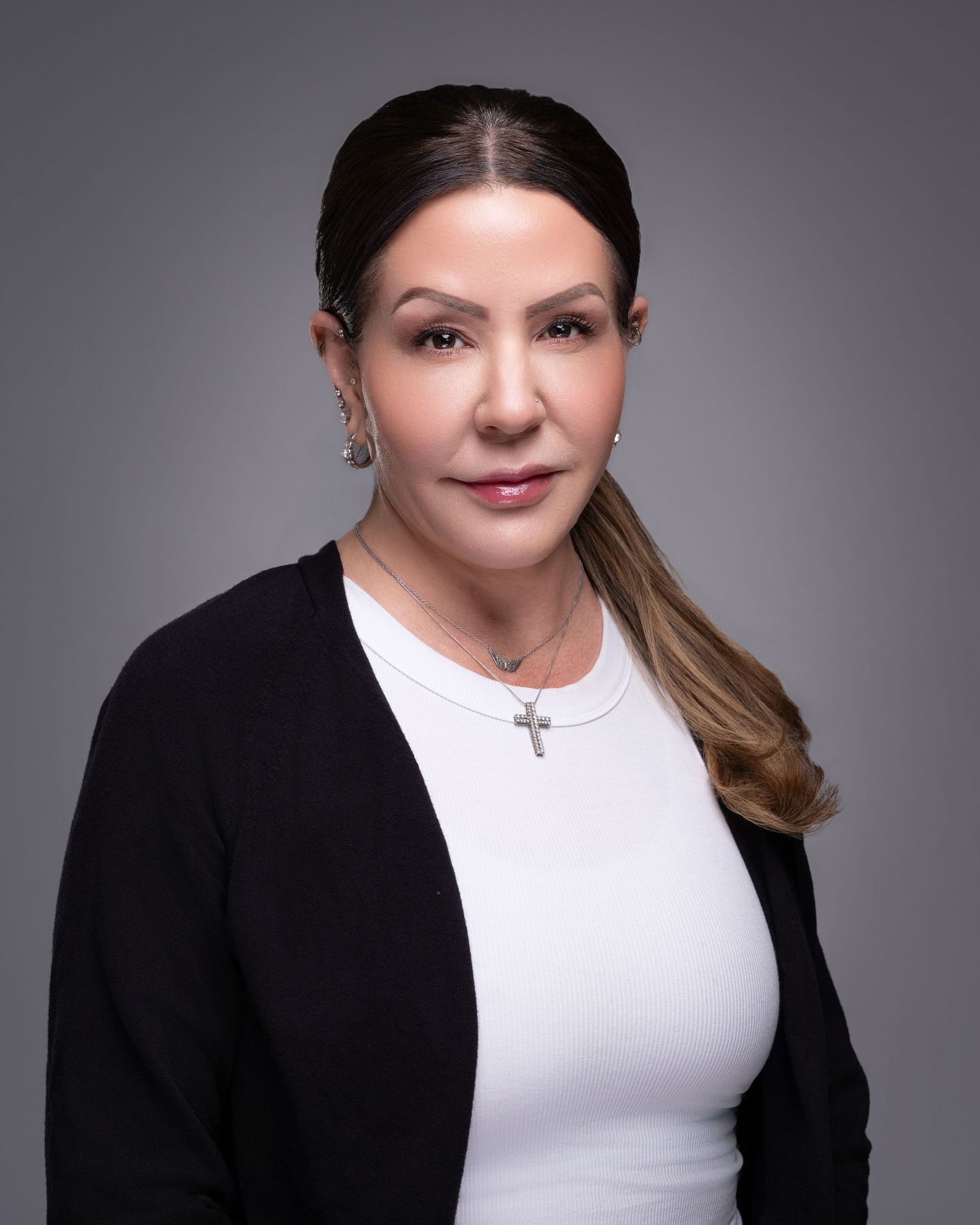 Professional headshot of woman in black cardigan and white top wearing cross necklace.