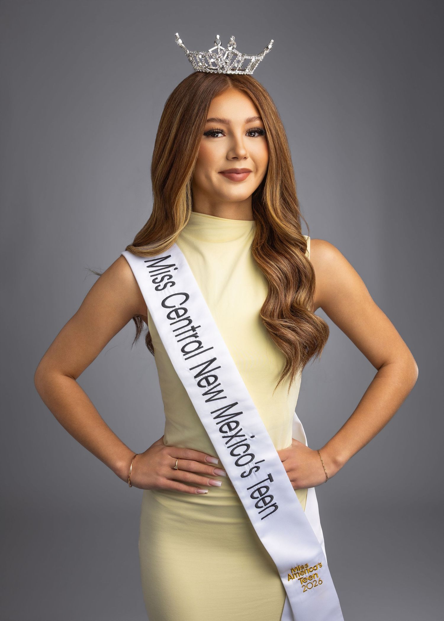 Young woman wearing Miss Central New Mexico Teen sash and crown in a light yellow dress poses confidently.