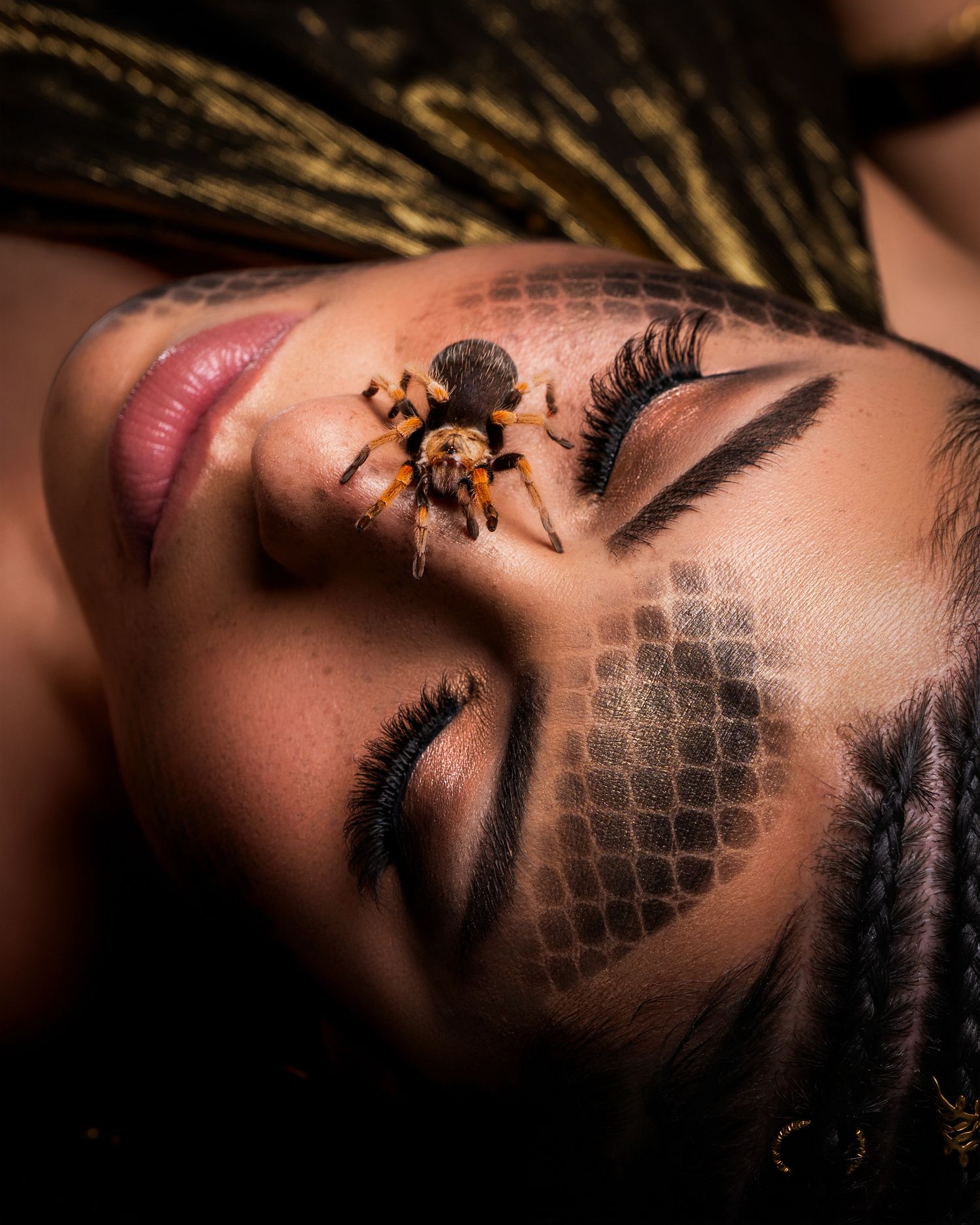 A woman with closed eyes and dramatic makeup has a tarantula spider resting on her face in an artistic photo.