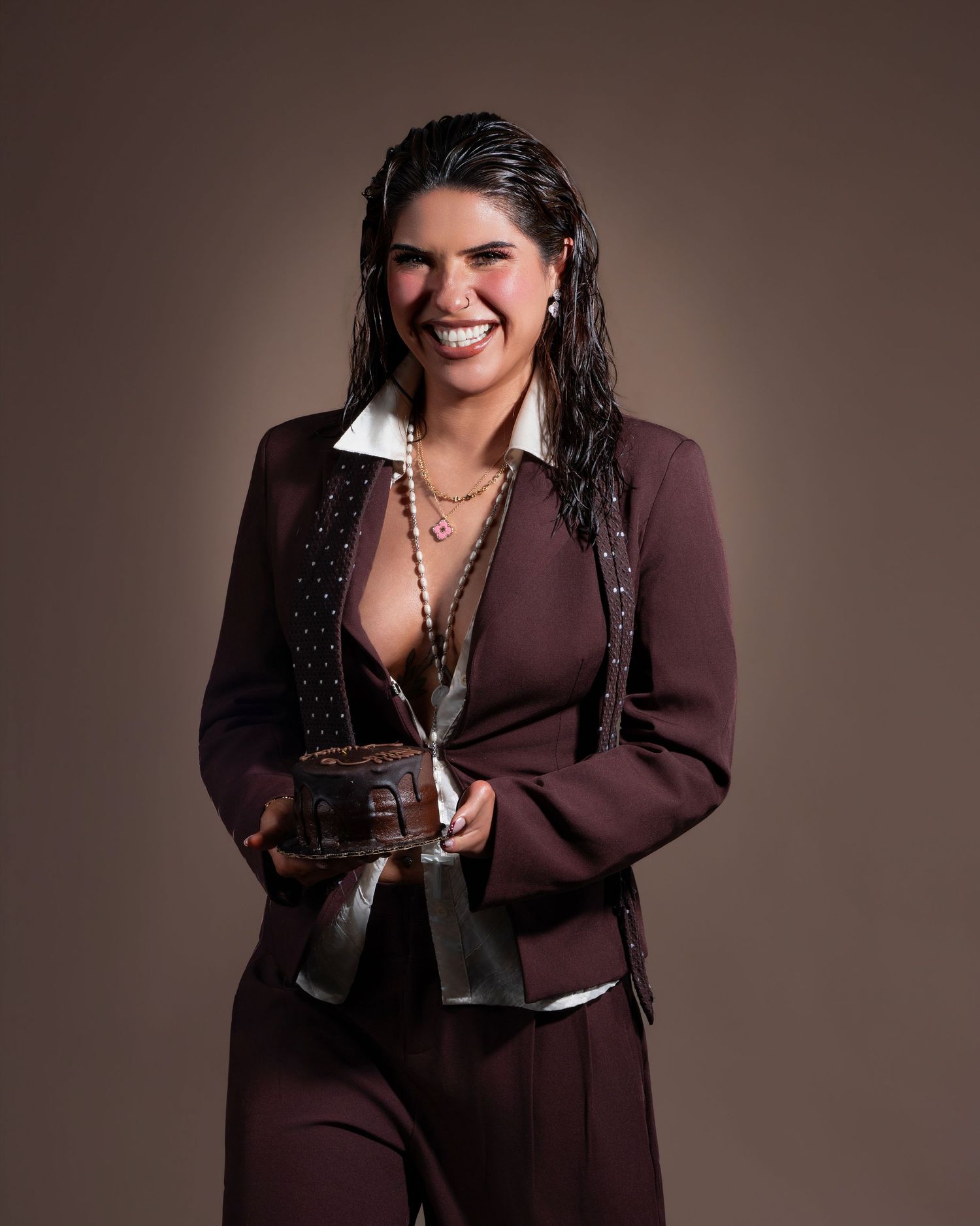 Woman in maroon suit smiling, holding a small trophy award against a brown studio background.