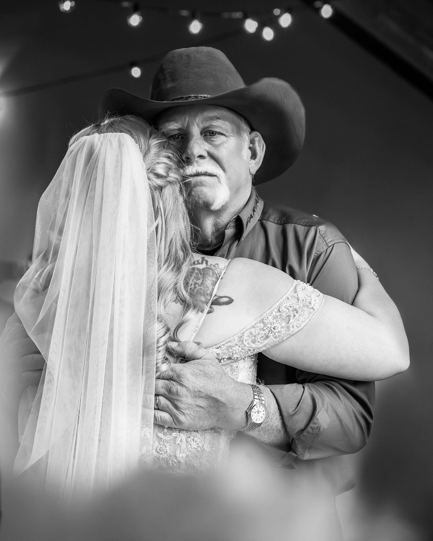 Emotional father-daughter dance at wedding, man in cowboy hat embracing bride in black and white.