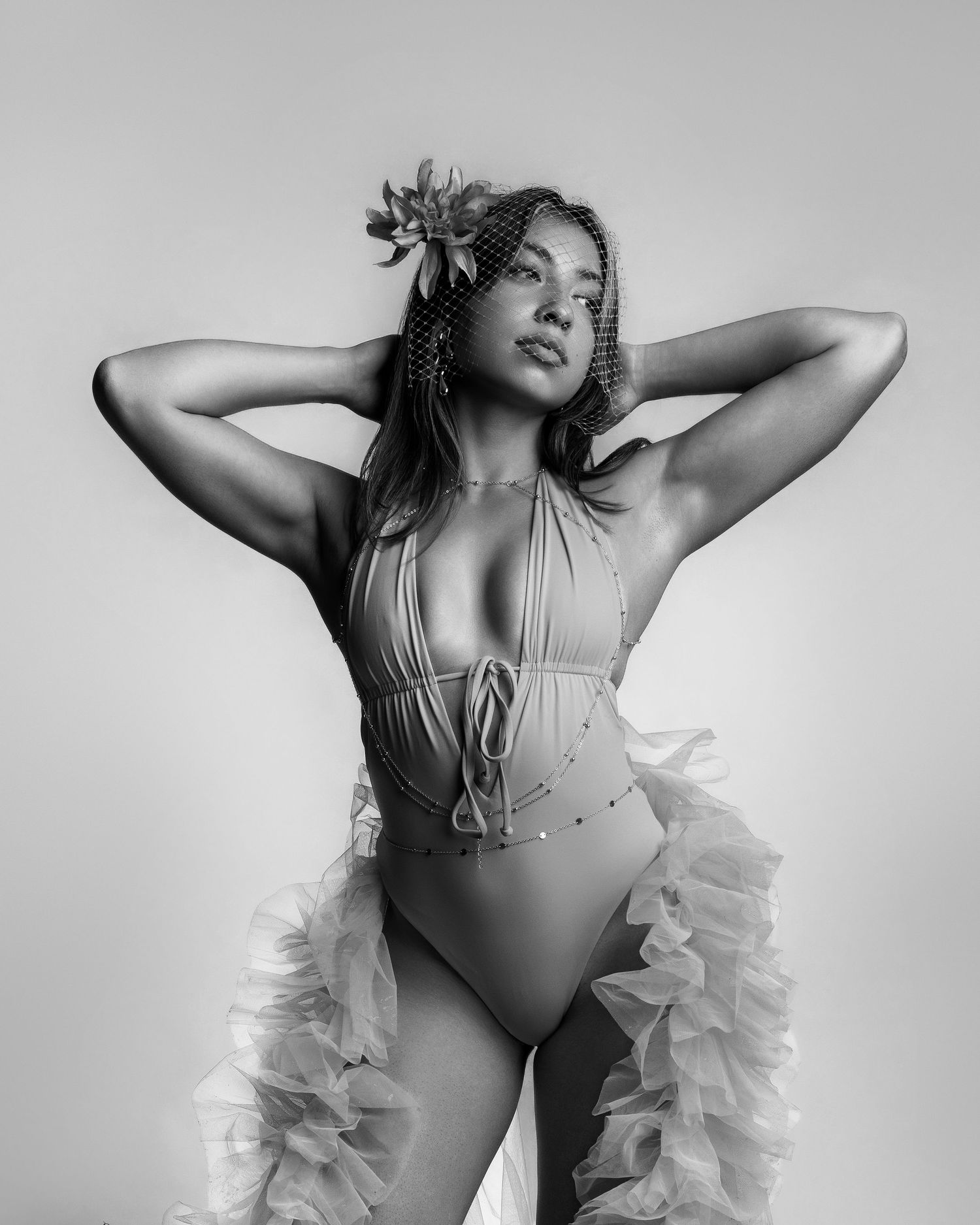 Black and white photo of a woman in a halter bodysuit with ruffled skirt and floral headpiece, posing gracefully.
