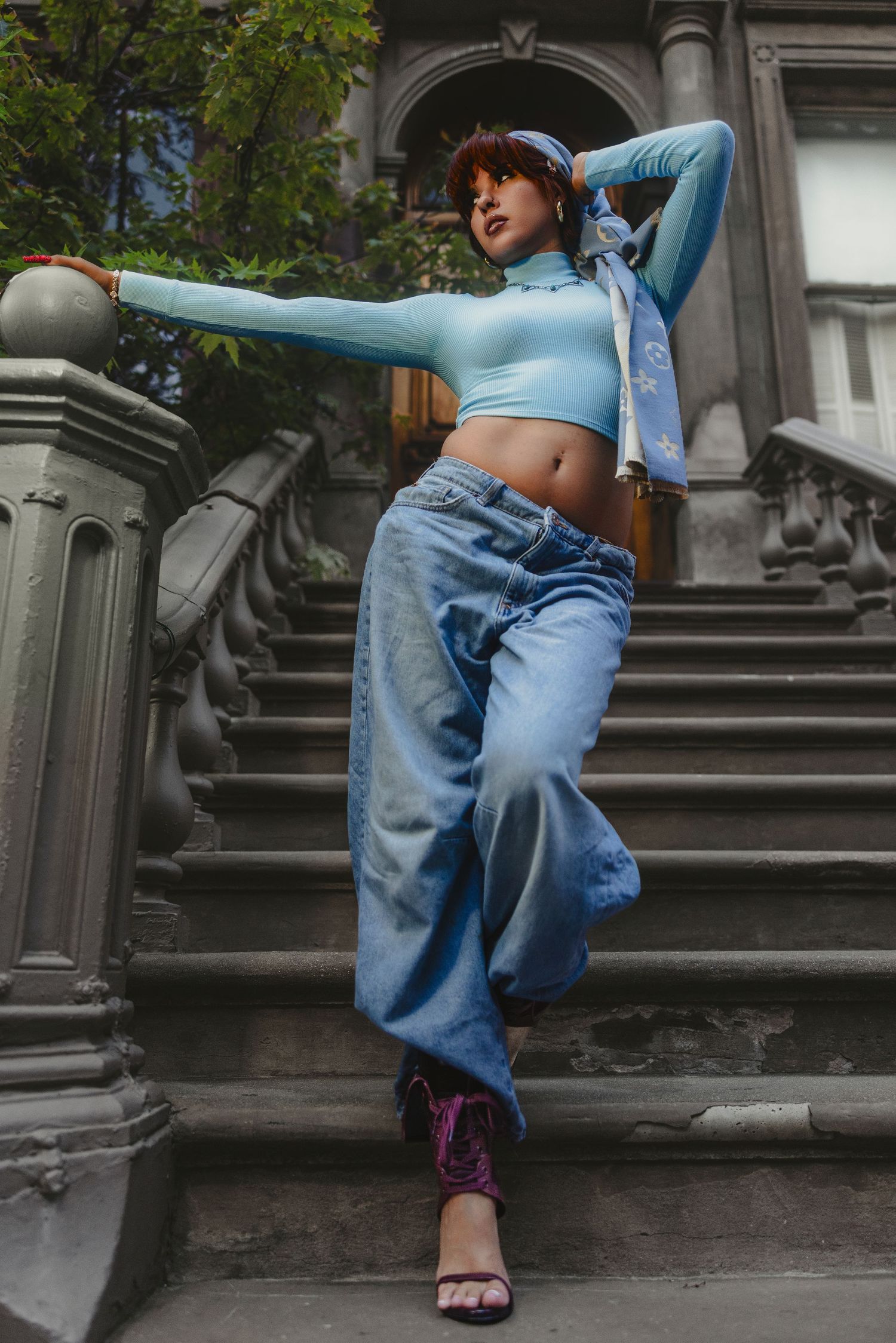 Woman in blue crop top and baggy jeans poses on stone steps outdoors.