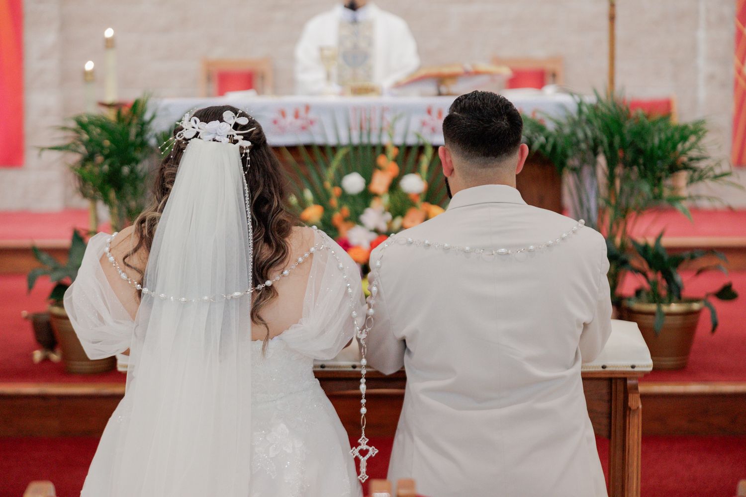 Bride and groom kneeling at altar during Catholic wedding ceremony, bride wearing white gown and veil.