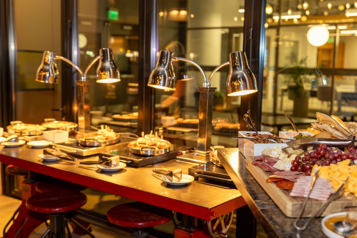 Elegant buffet spread with heat lamps over gourmet dishes and charcuterie board at upscale restaurant.