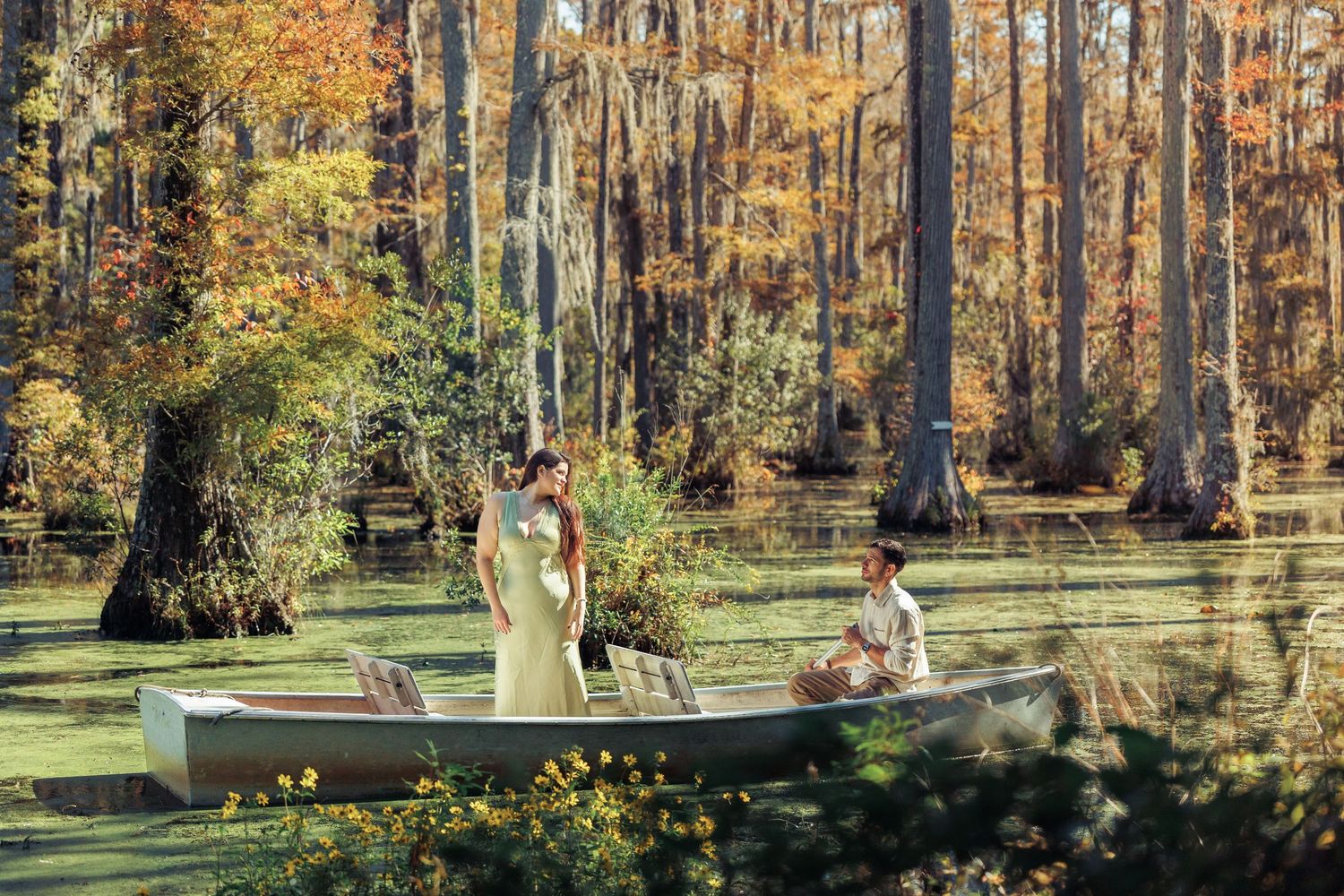 Couple in a rowboat on a serene cypress swamp surrounded by autumn foliage in golden light.