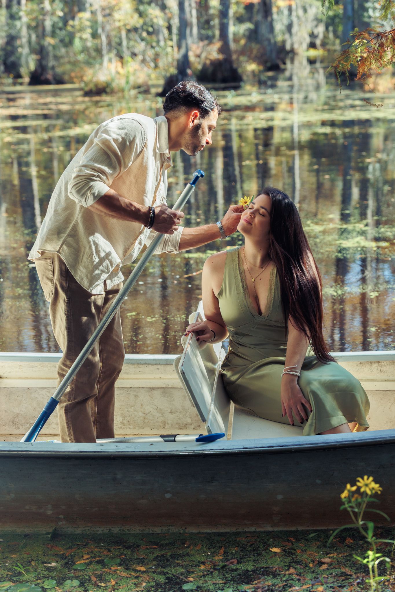 A romantic couple in a rowboat on a serene lake, man placing a flower in woman's hair.