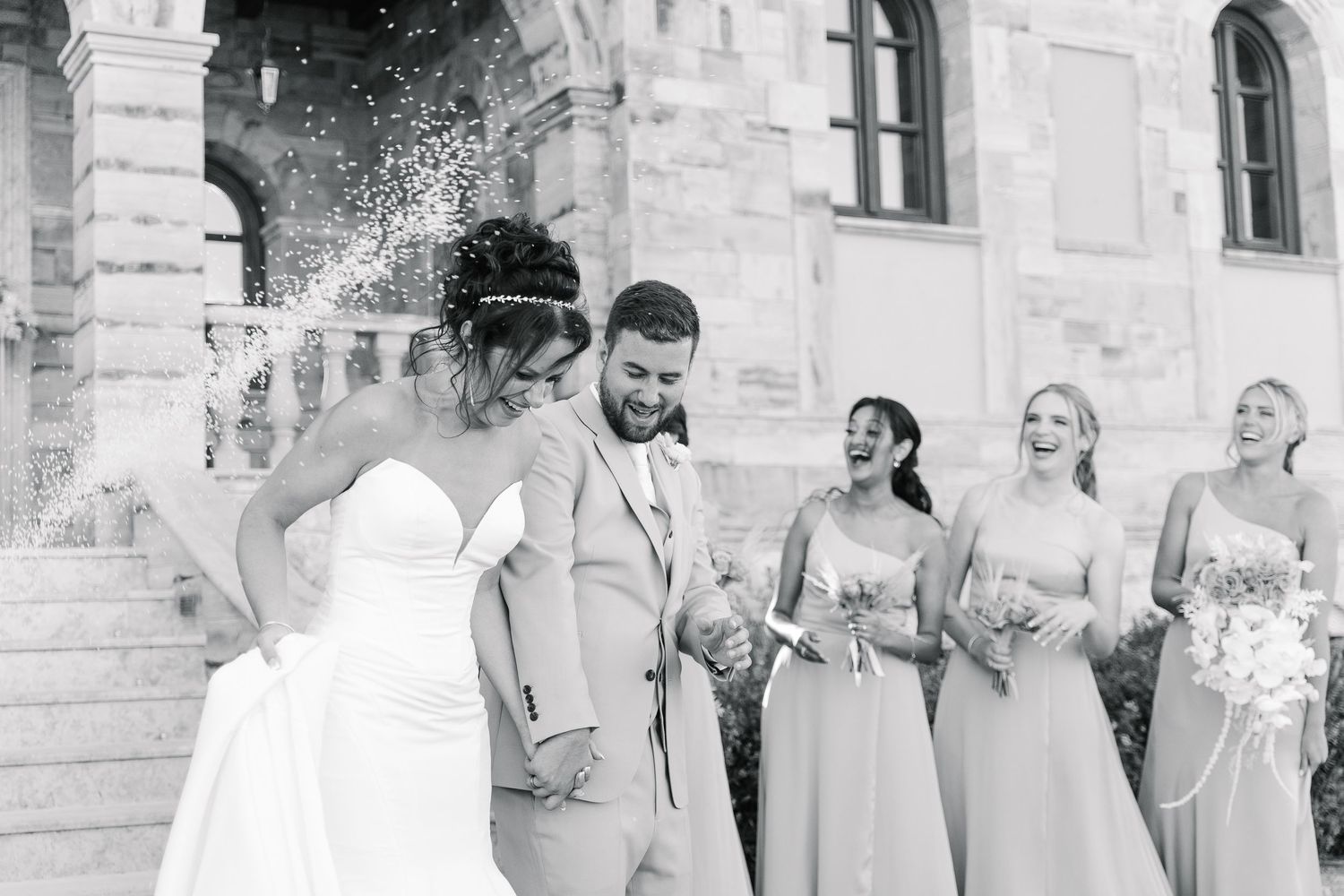 Black and white candid wedding photo with bridal party on stone steps.