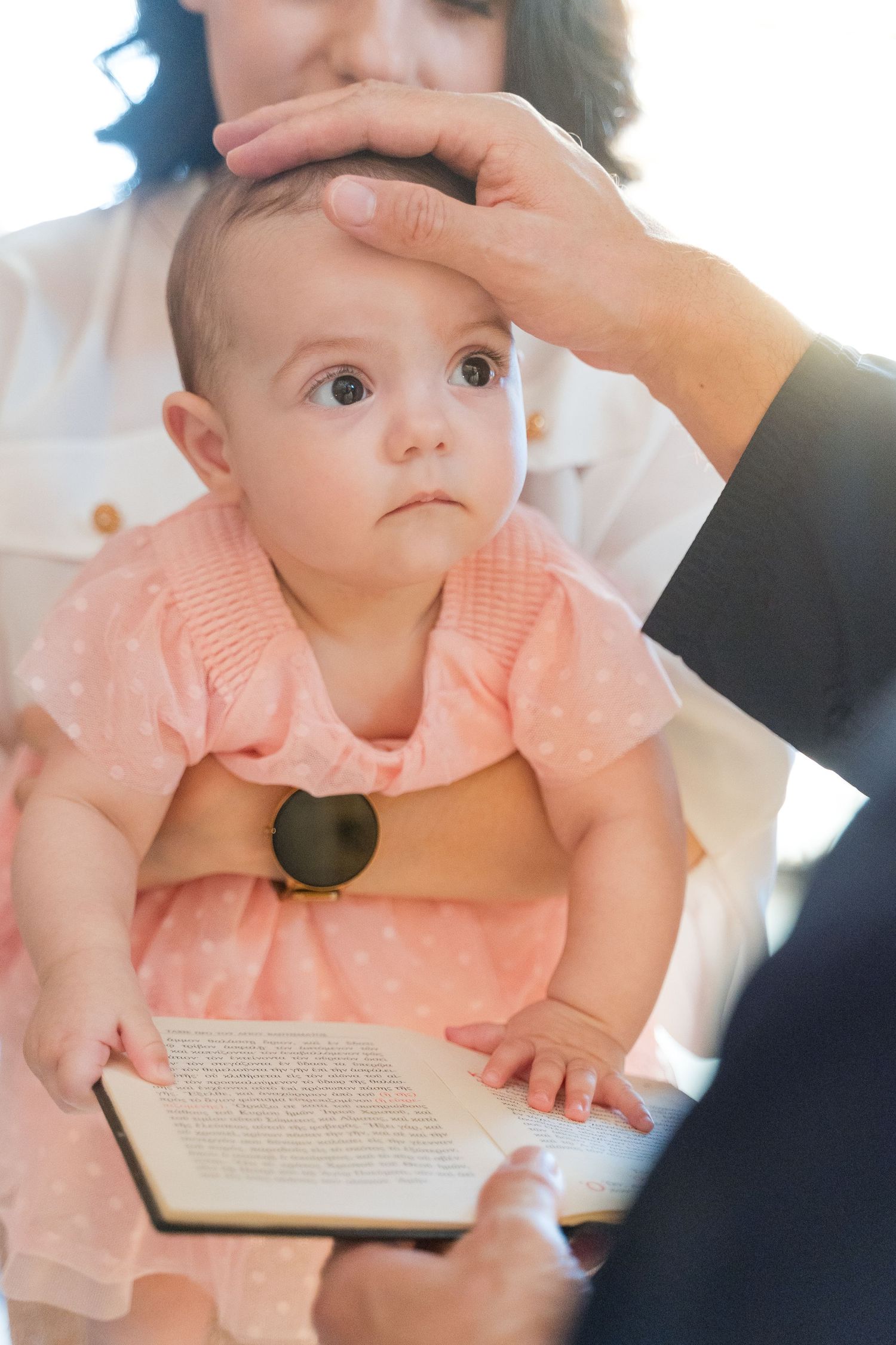 Baby in a peach-colored dress examines book pages while sitting with caregiver.