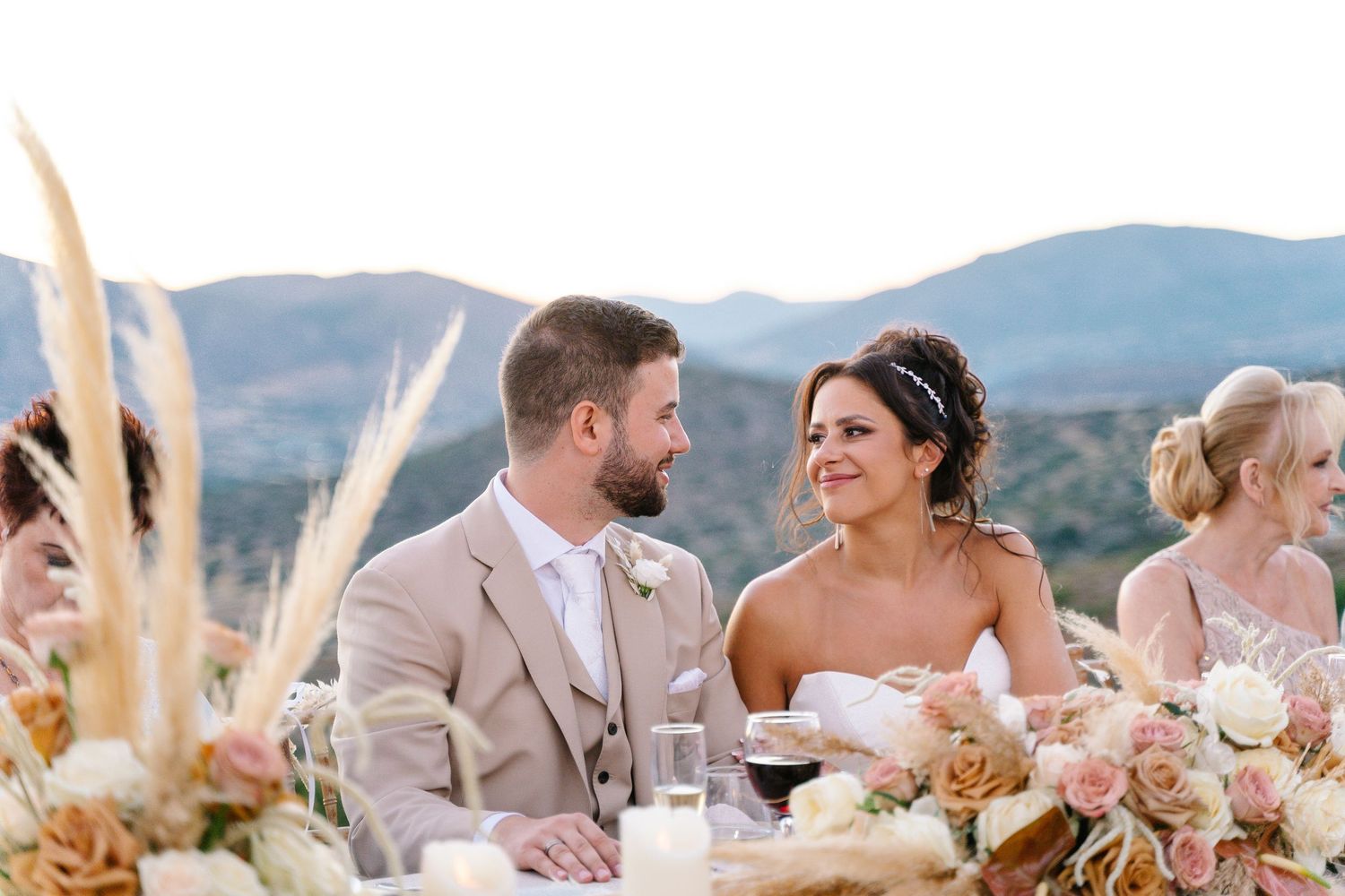 Wedding reception table settings with pampas grass decor against mountain backdrop.