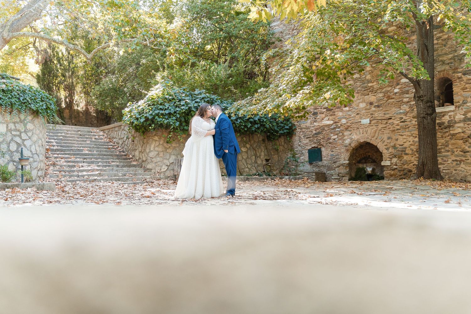Wedding couple walking along a rustic stone path surrounded by autumn foliage.