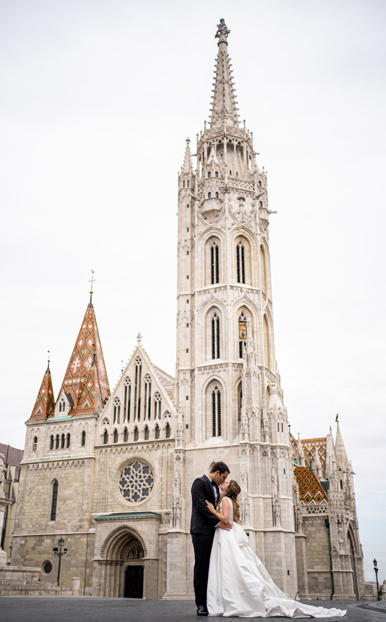 Three romantic photos of a couple at the ornate Gothic Matthias Church in Budapest with its white stone spires and towers.