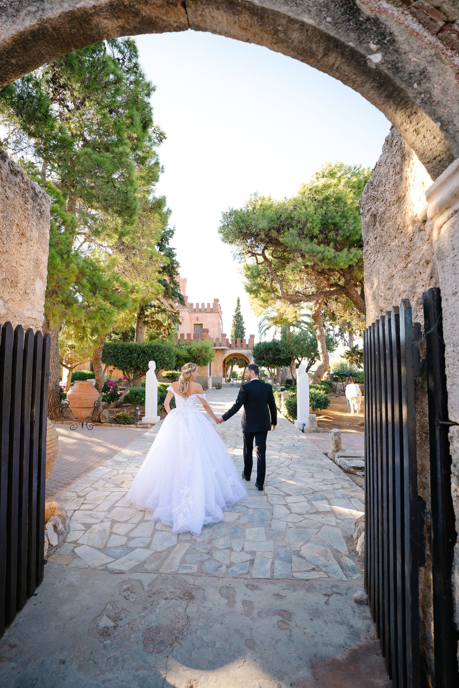 Couple walks through stone archway in Mediterranean garden setting during their wedding day.