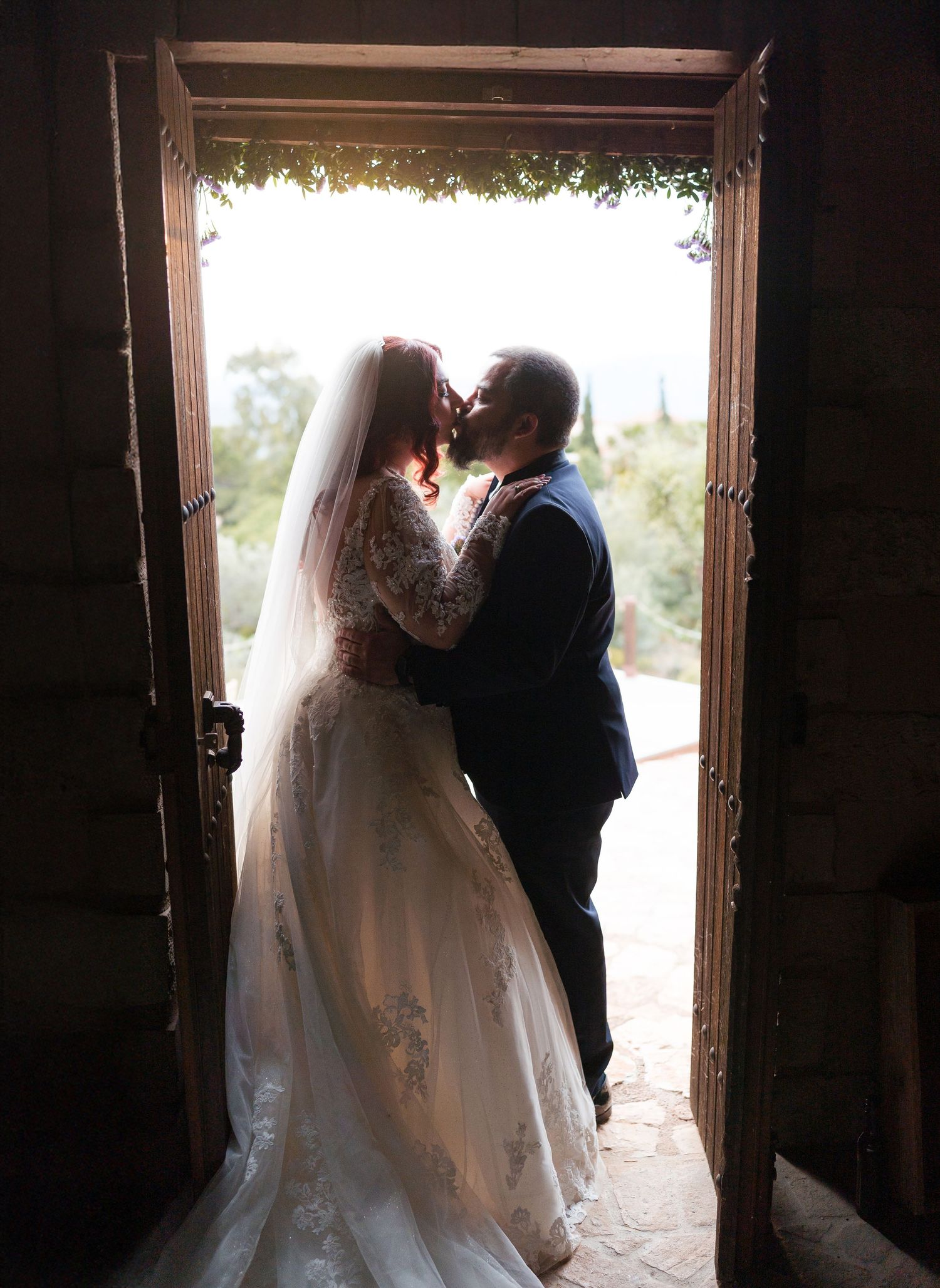 Romantic silhouettes of newlyweds standing in backlit doorway during wedding photography session.