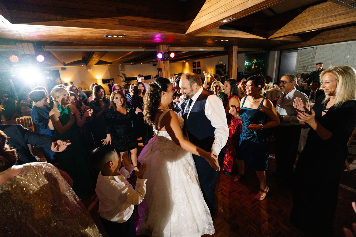 Wedding reception guests dance together on a dimly lit dance floor during evening celebrations.