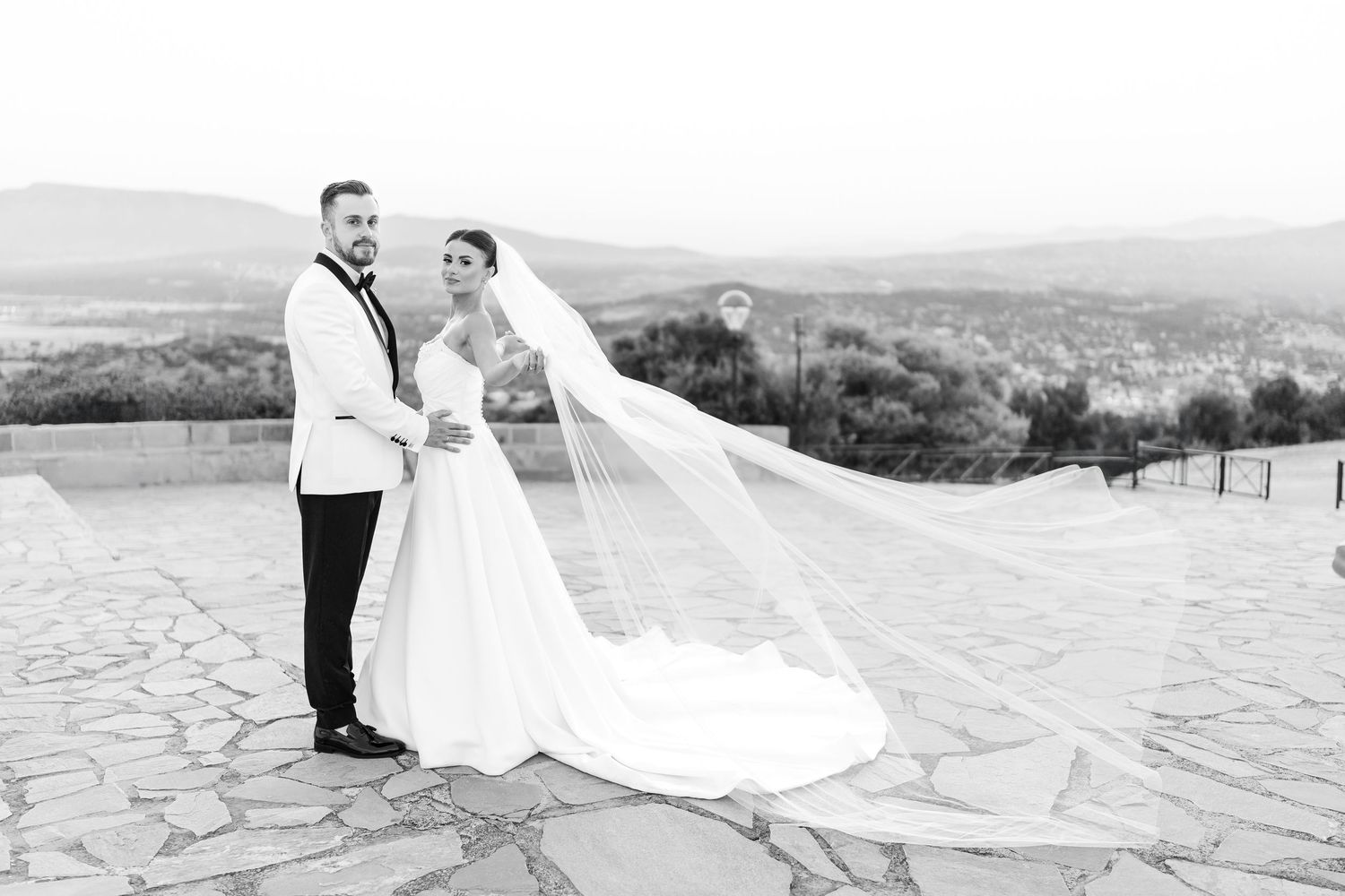 A couple in wedding attire walks along a scenic stone path during an elegant outdoor photo session.